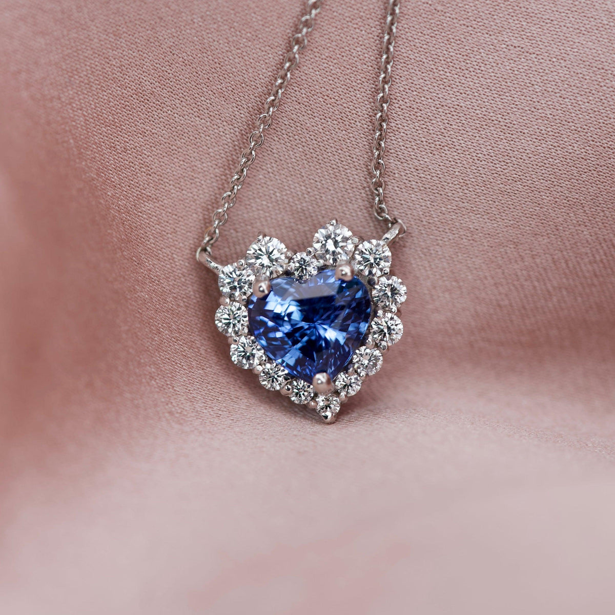 Macro shot of a custom sapphire heart necklace with a graduated diamond halo on silk