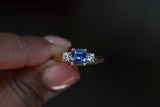 Three stone sapphire engagement ring featuring Ceylon blue sapphire center with brilliant cut diamond side stones in yellow gold setting