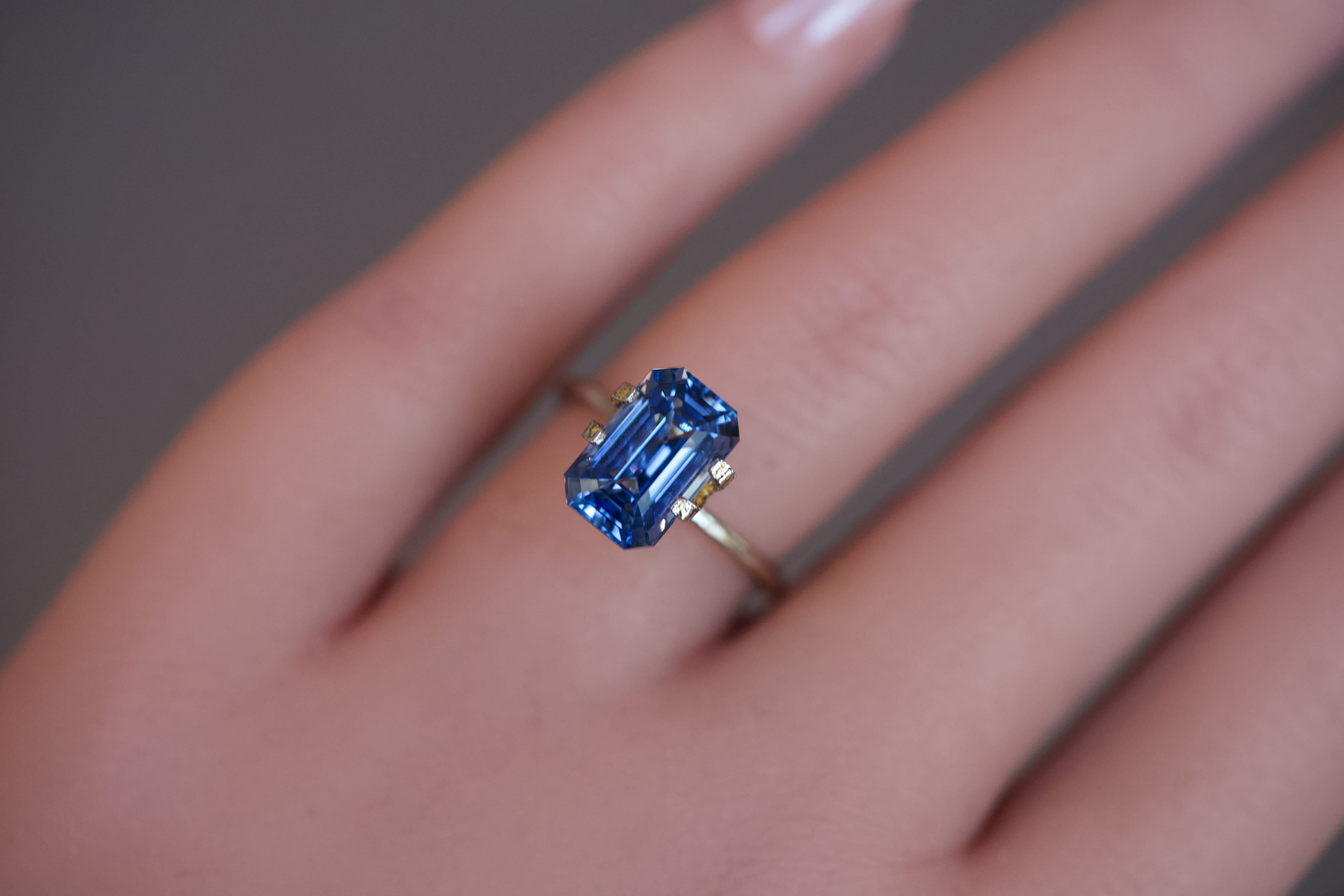A heated blue octagonal sapphire set in a gold mock-up ring on a model's hand.