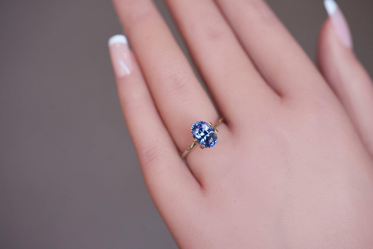 An elegant, unheated bluish-violet oval sapphire set in a temporary gold ring on a hand.