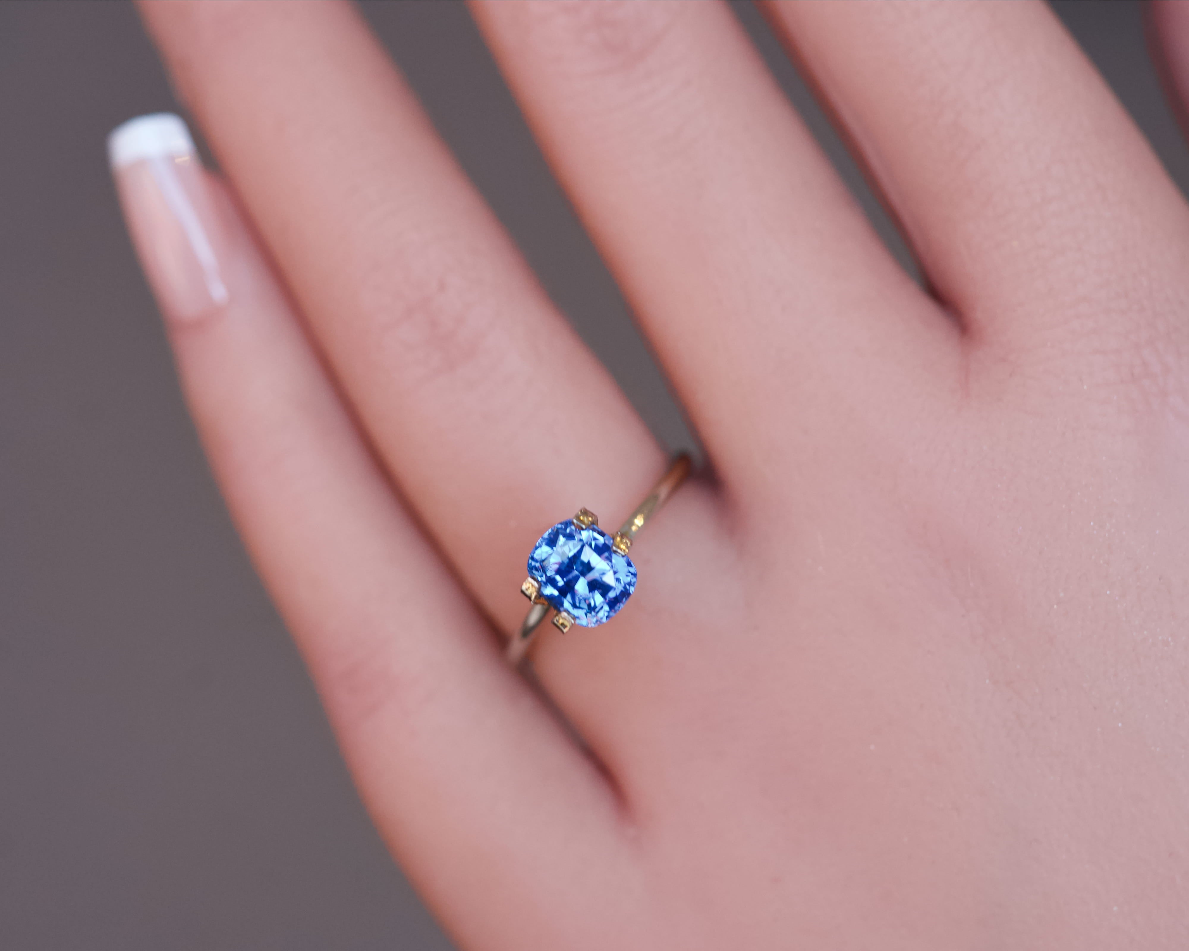 Detailed view of a vibrant blue Ceylon cushion sapphire worn in a temporary gold ring.