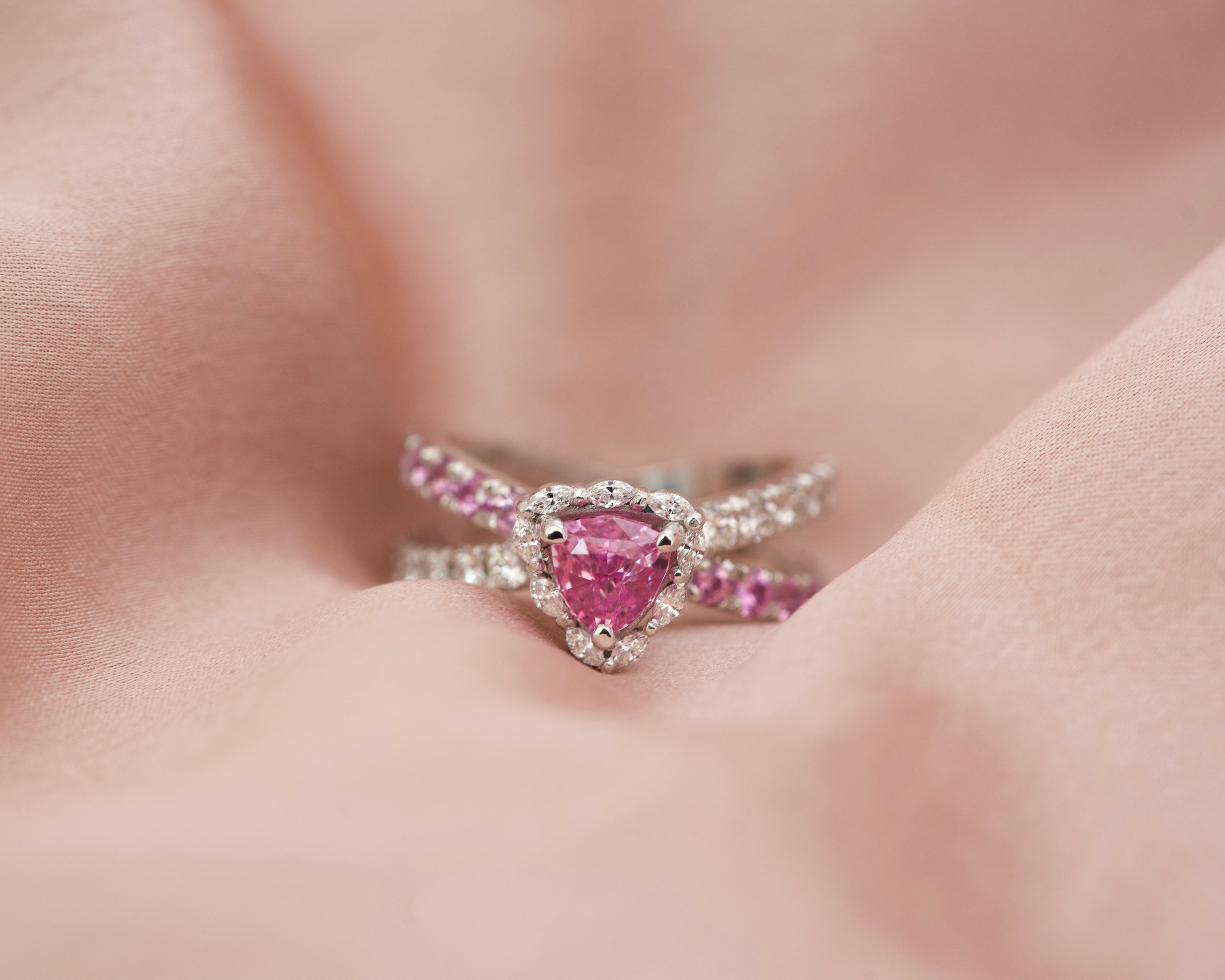 Luxury pink sapphire and diamond halo ring resting on pink silk fabric