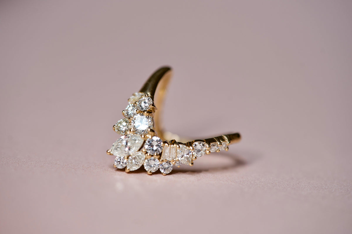 Luxury curved diamond cluster wedding band with marquise and round diamonds on a soft pink background