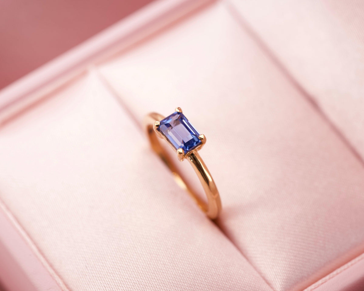 A luxury east-west blue sapphire solitaire ring presented in a signature pink velvet box
