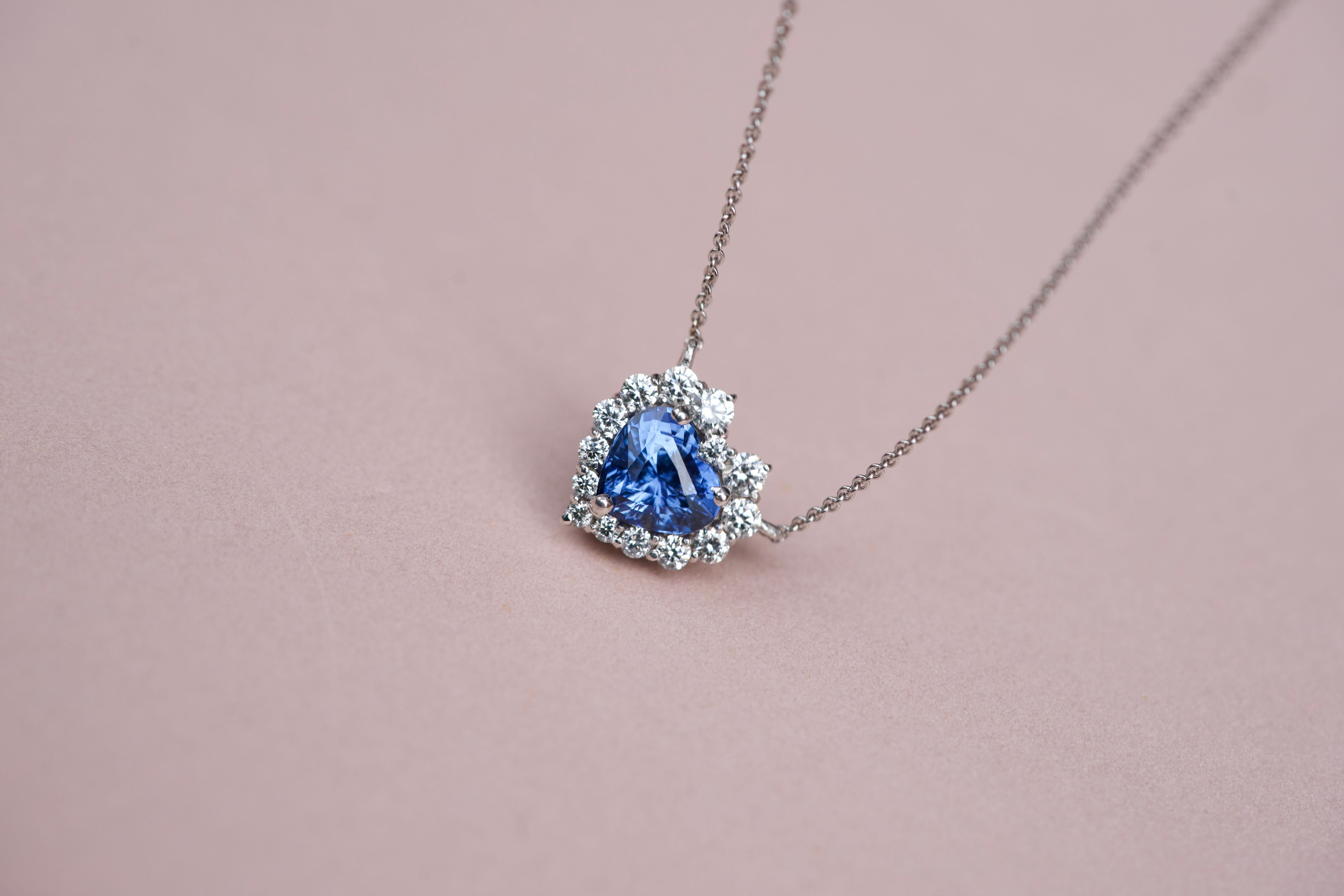 Elegant blue sapphire heart pendant with graduated diamond border against a soft pink backdrop