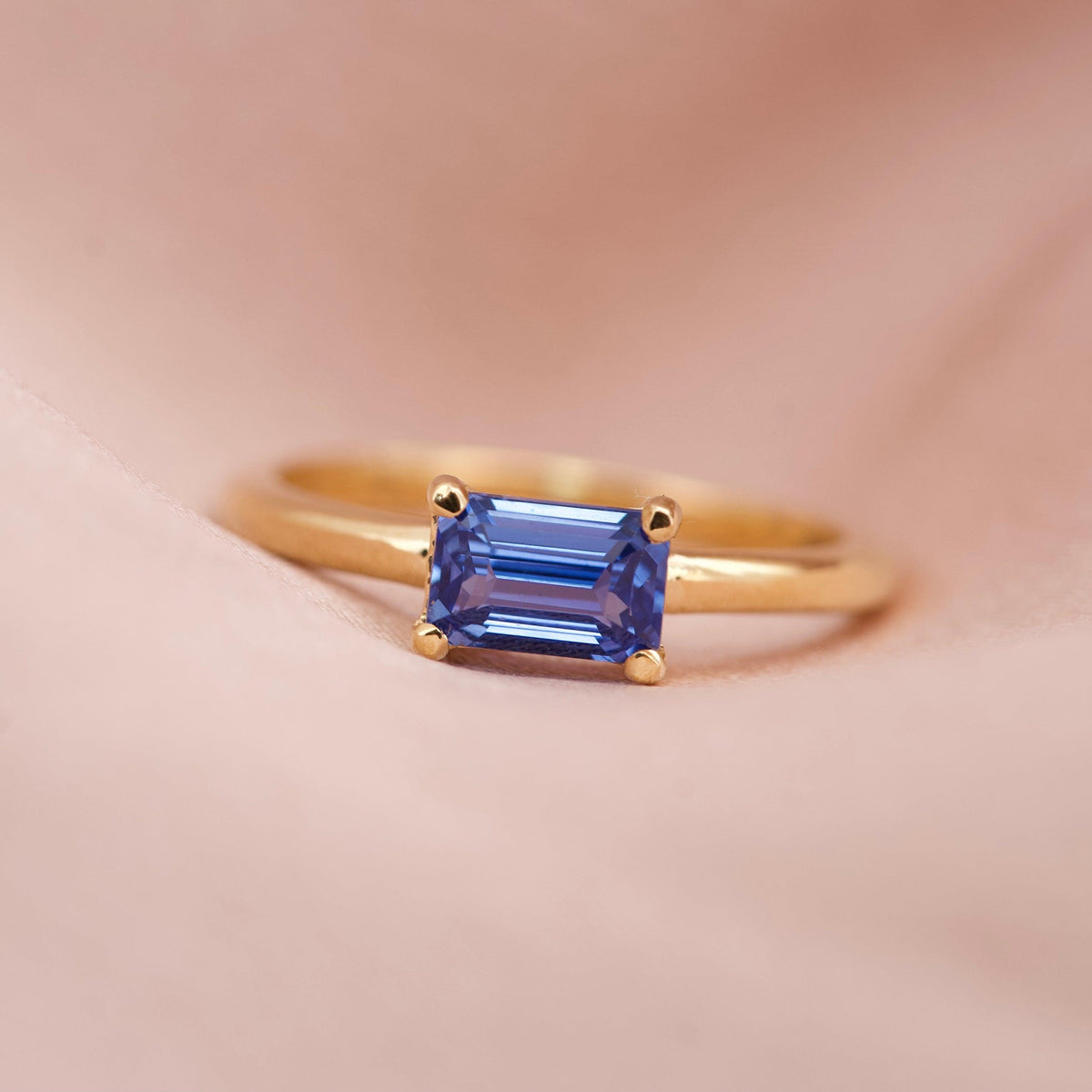 A vivid cornflower blue emerald cut sapphire set horizontally in an 18k yellow gold solitaire ring