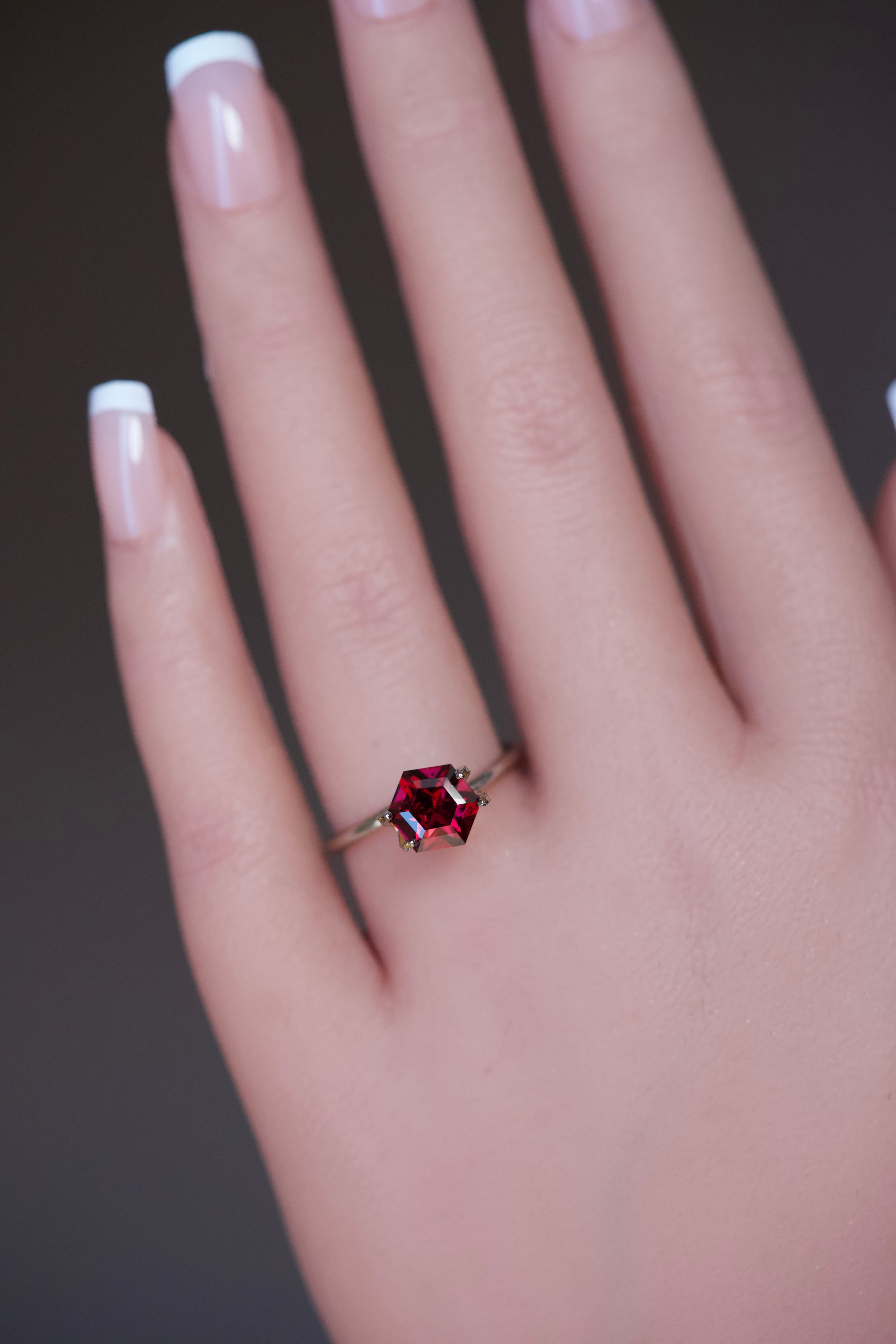 A uniquely geometric fancy-cut purplish pink garnet stone resting on a hand.