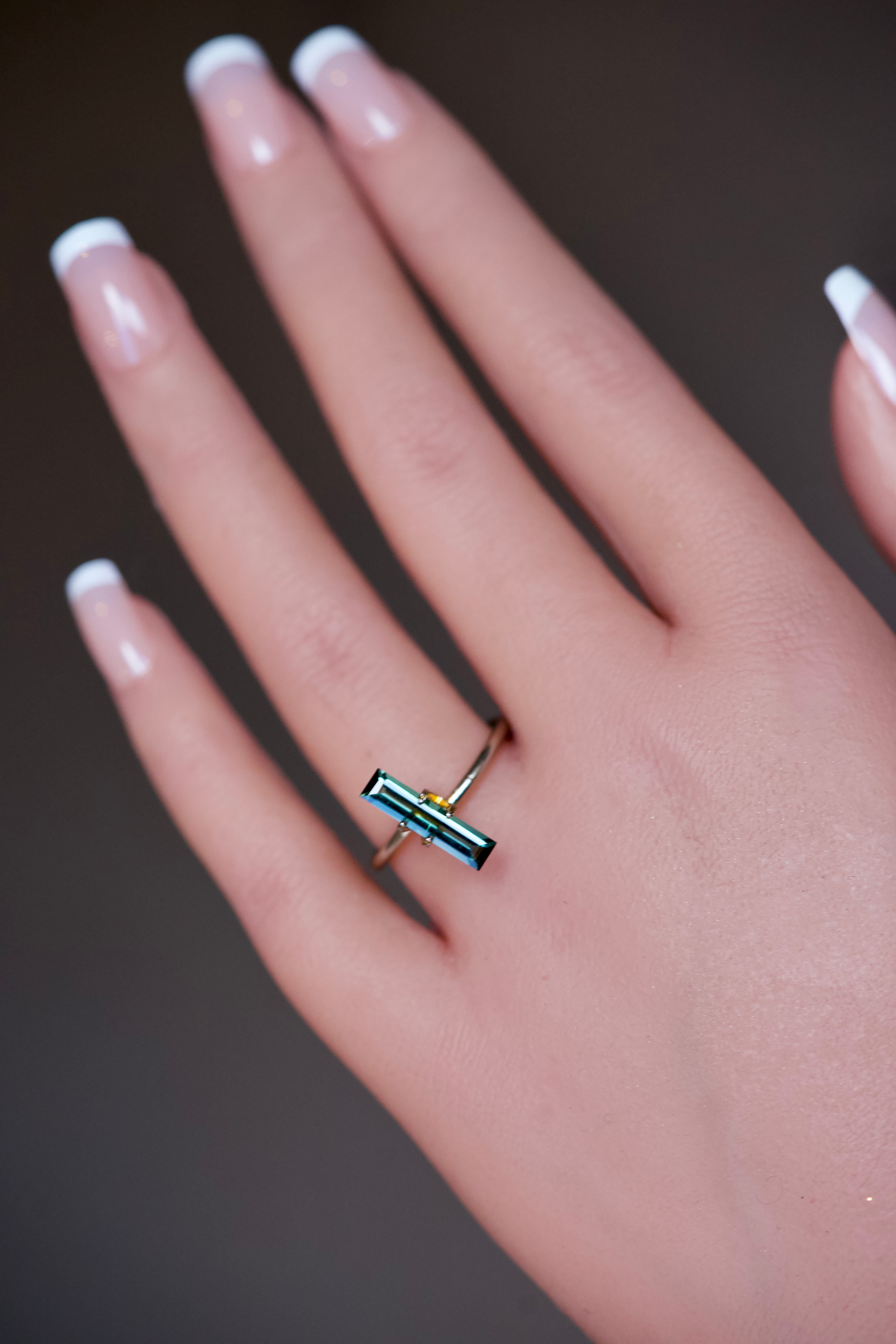 Elongated green tourmaline set horizontally in a gold ring mockup on a hand.