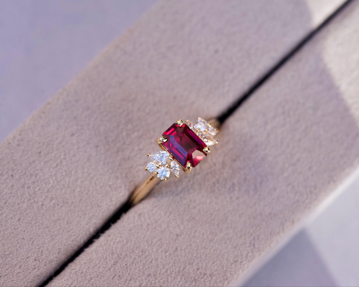 Overhead wide view of a step cut ruby cluster ring nestled inside a grey luxury box