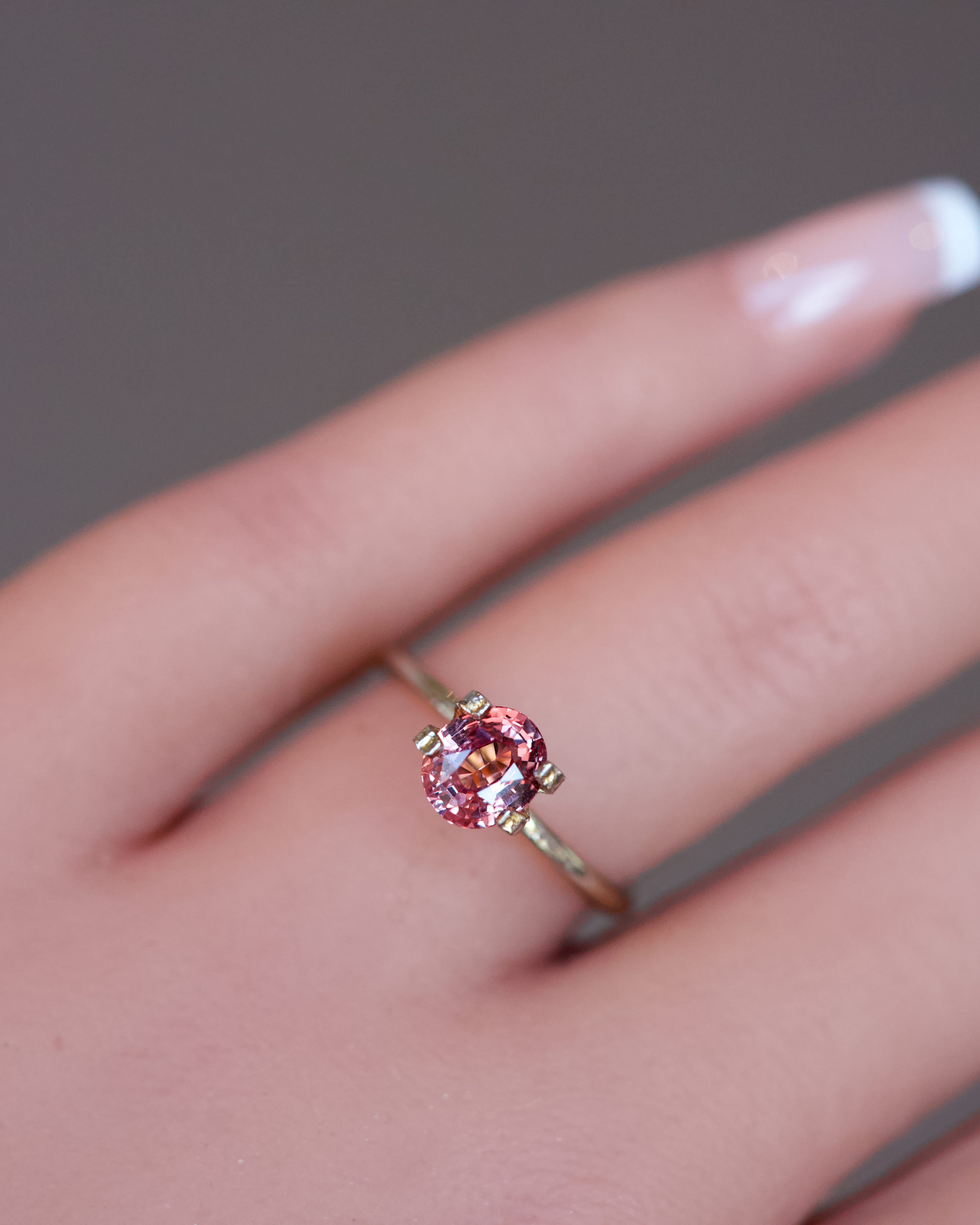 Detailed view of a natural, heated Padparadscha sapphire resting in a temporary ring setting, showcasing its sunset-like colour.