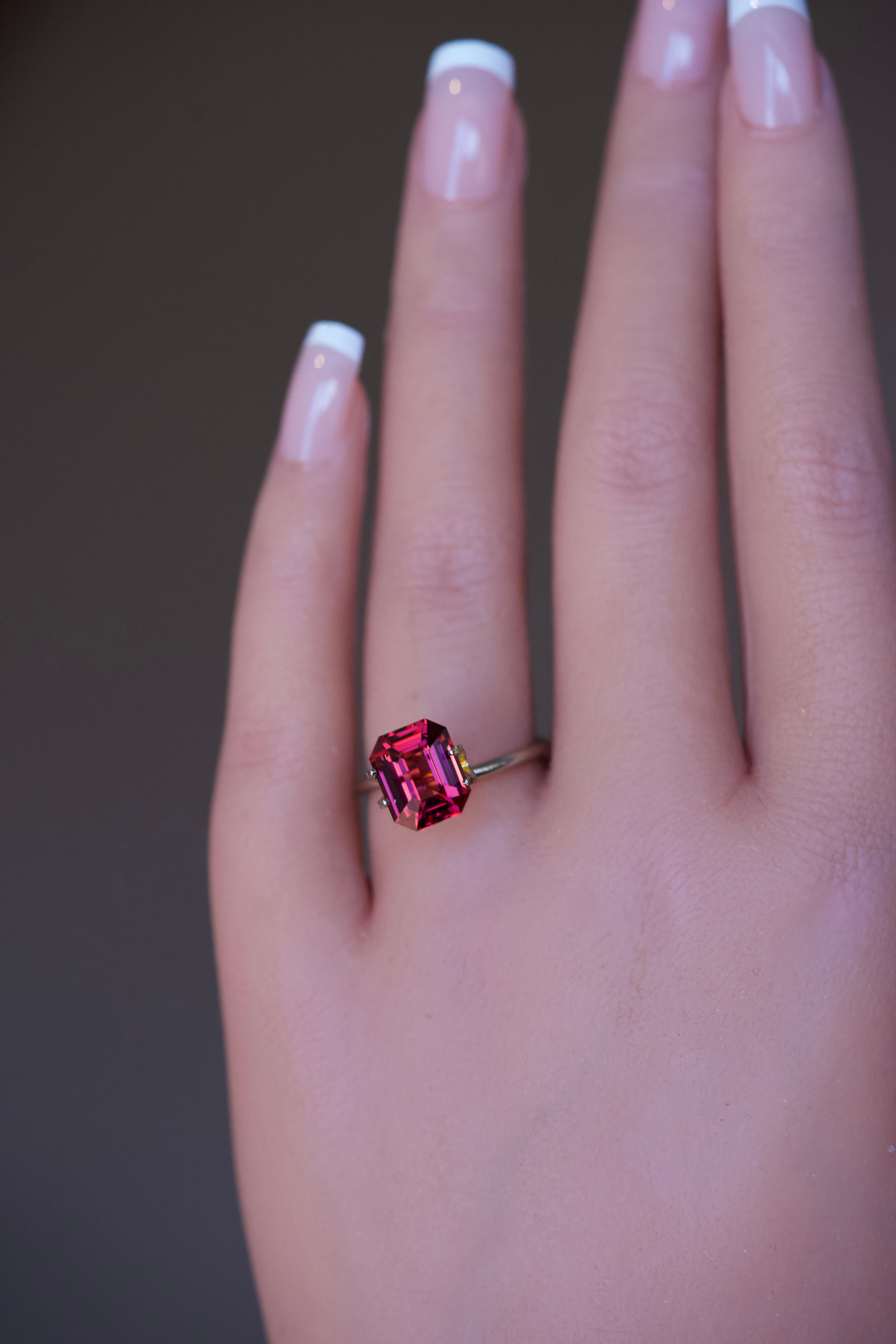 Orangish pink rhodolite garnet in a gold ring mockup on a hand.