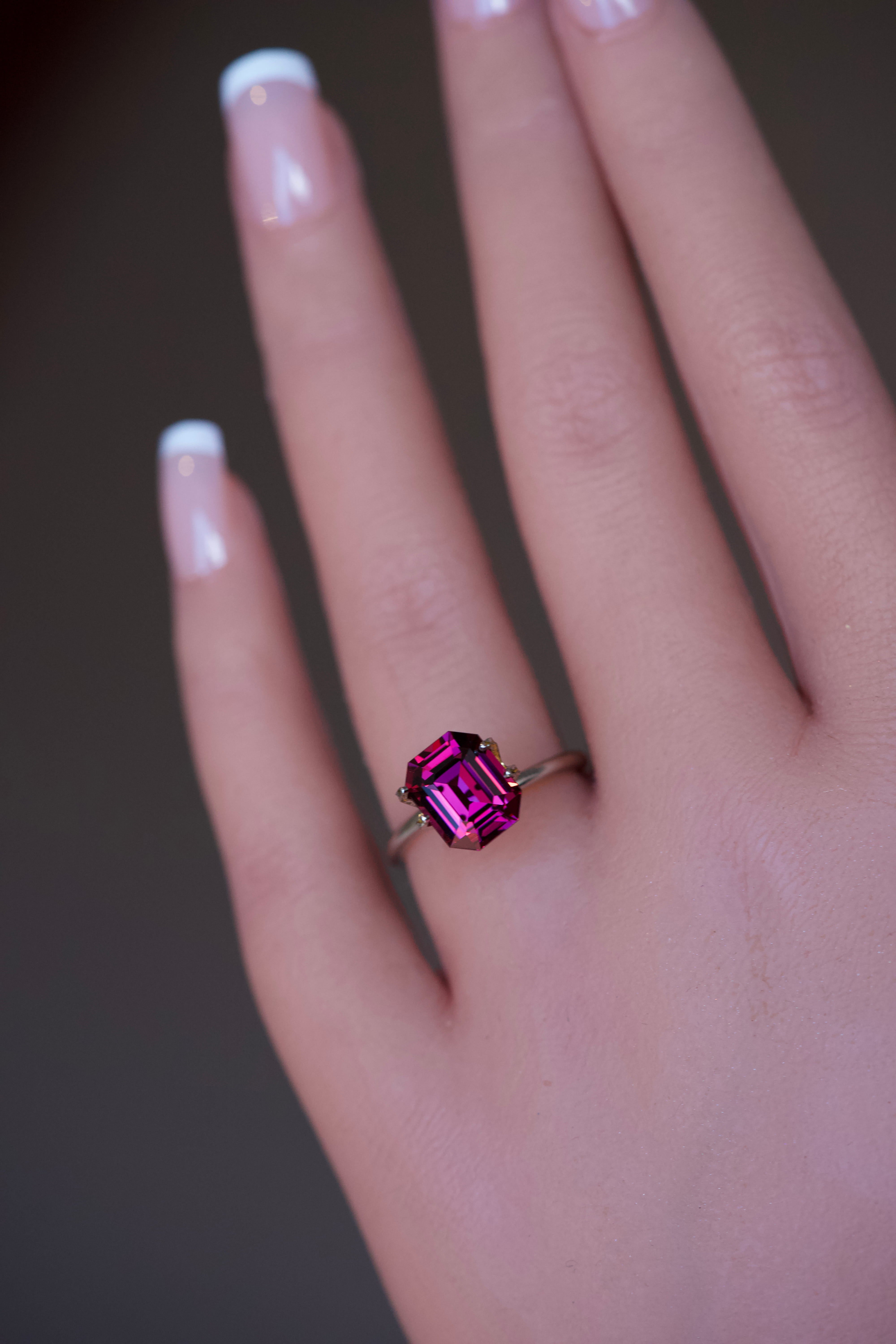 Purplish pink rhodolite garnet in a gold ring mockup on a hand.