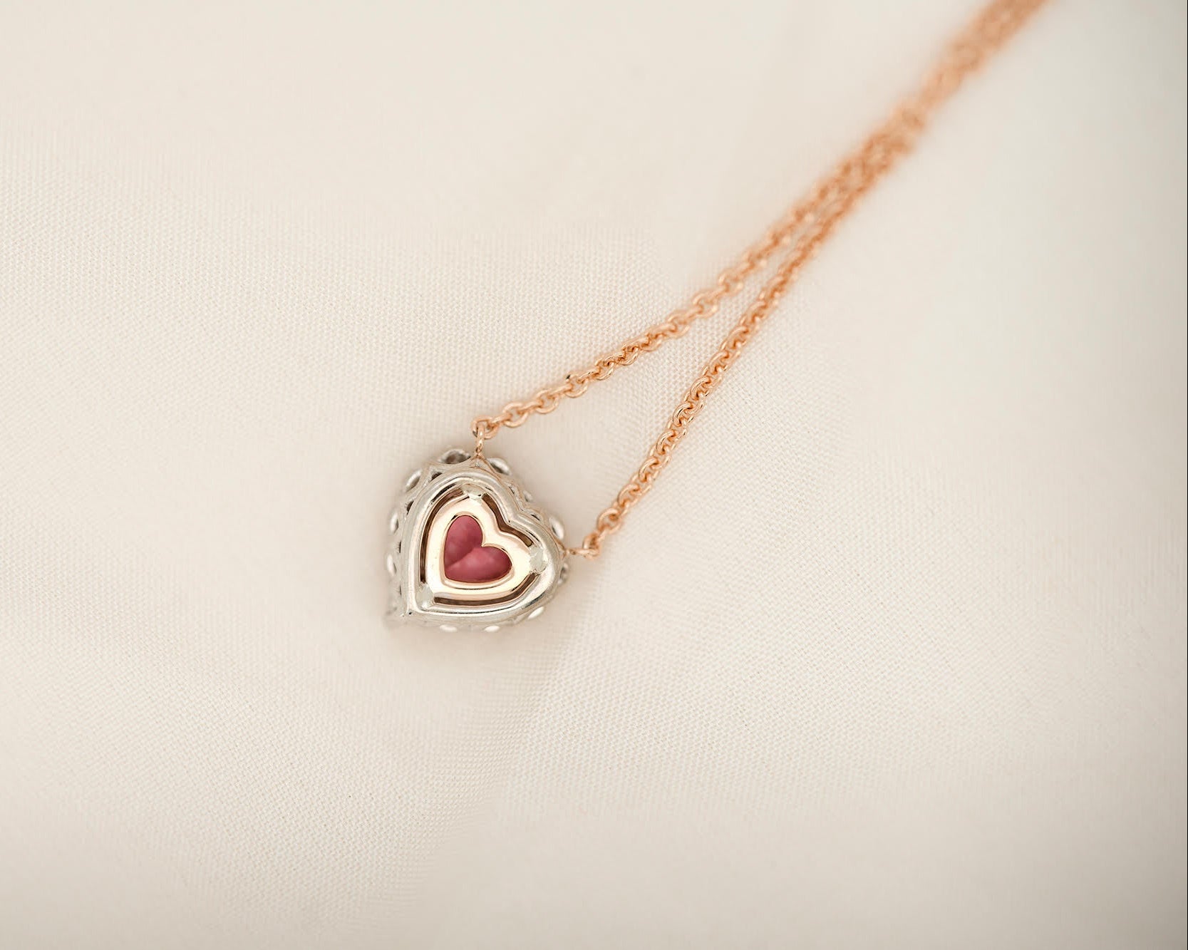 Heart-shaped padparadscha sapphire necklace on soft white fabric.