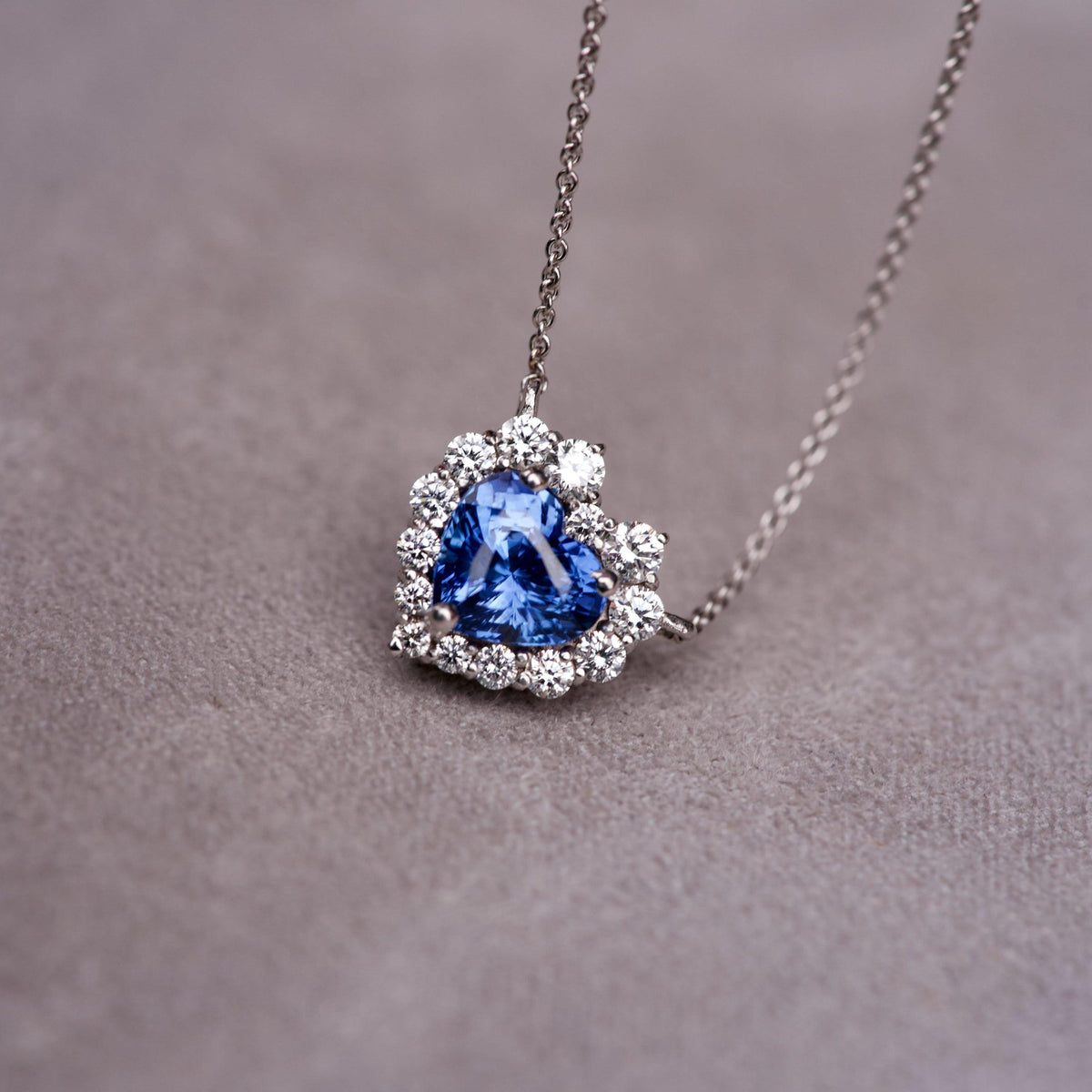 Heart shaped blue sapphire pendant with a sparkling graduated diamond halo on a grey textured surface