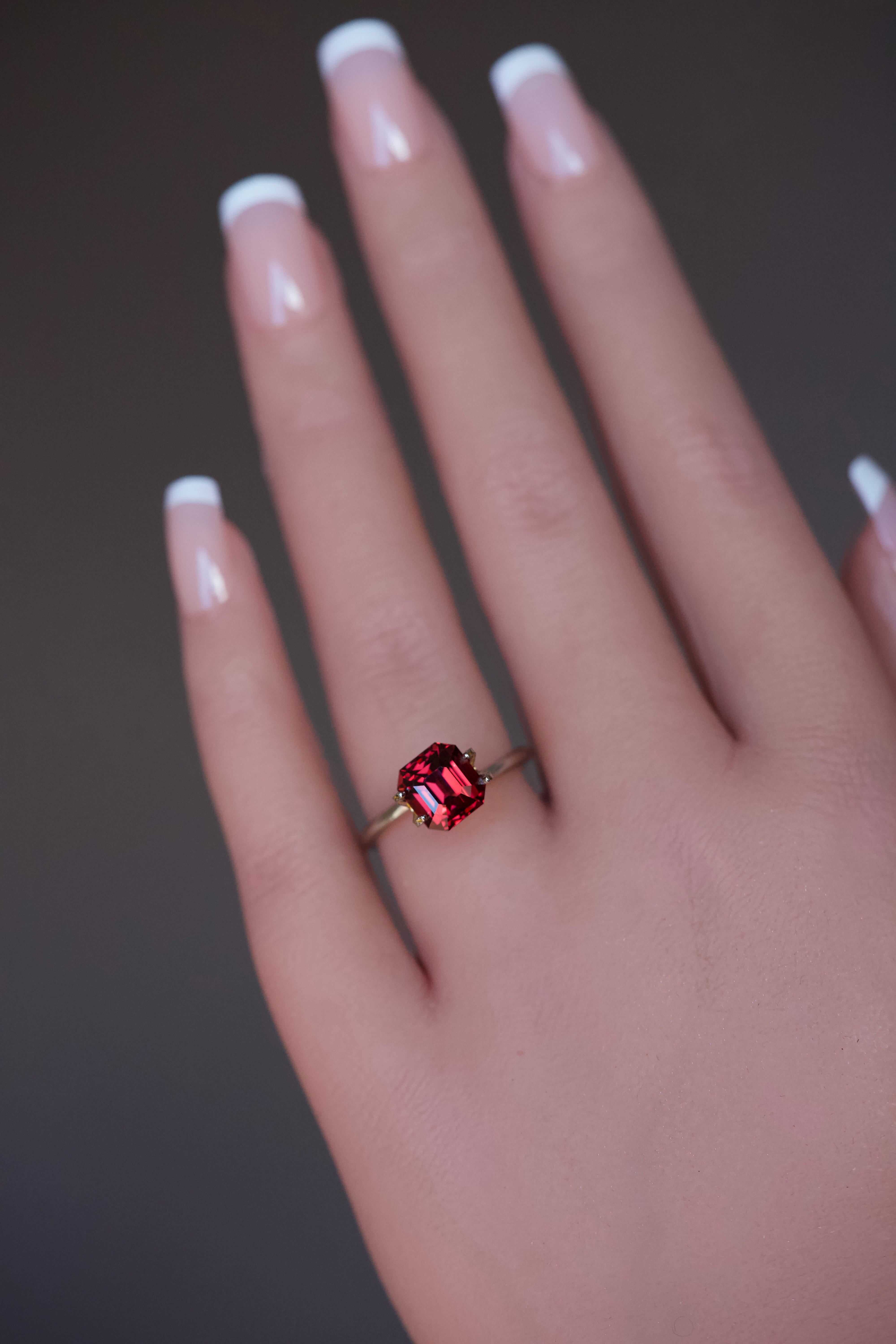 Model trying on an octagonal orangish pink garnet ring.