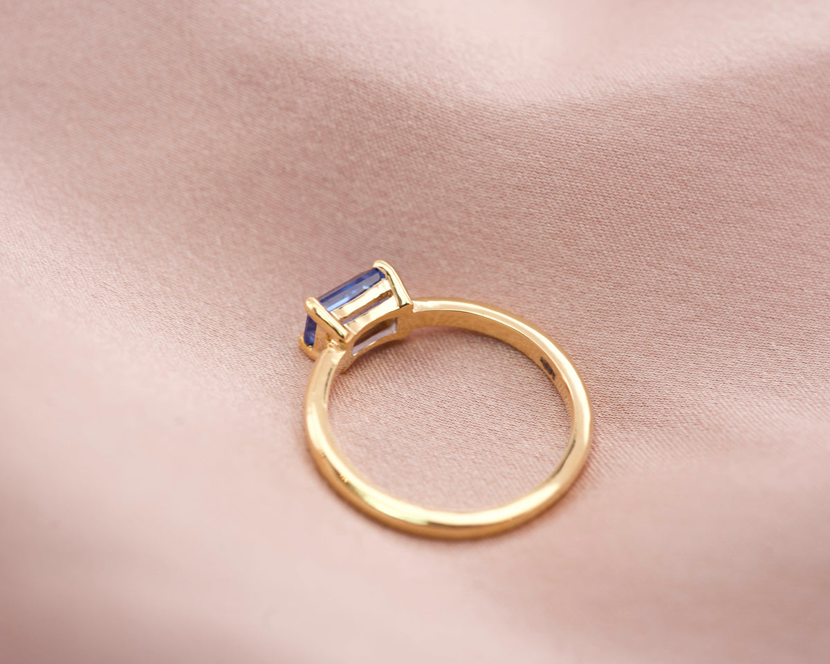 Side view of a low profile emerald cut blue sapphire ring showing the 18k yellow gold band