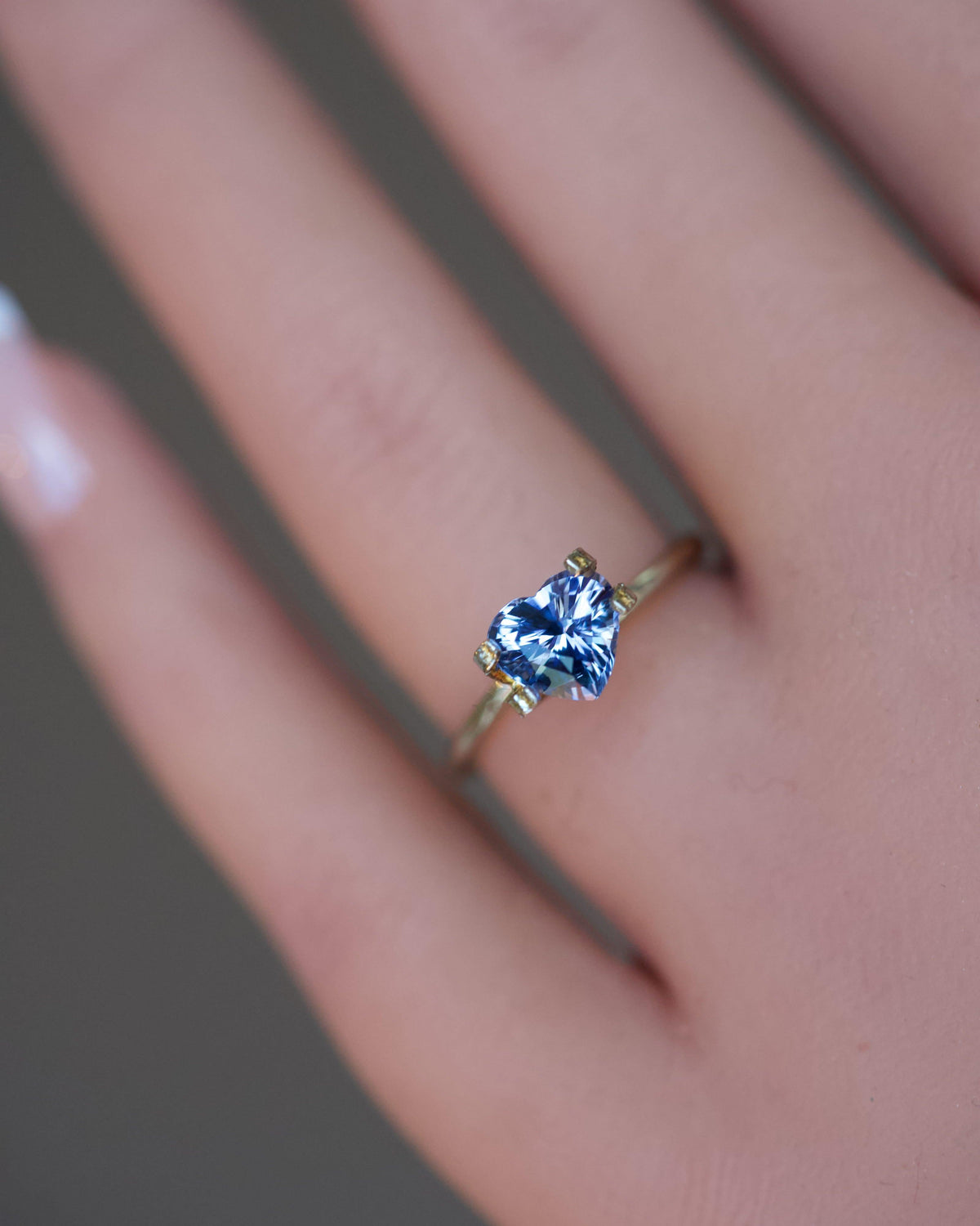 A romantic, unheated bluish-violet heart-shaped sapphire displayed in a temporary gold ring on a finger.