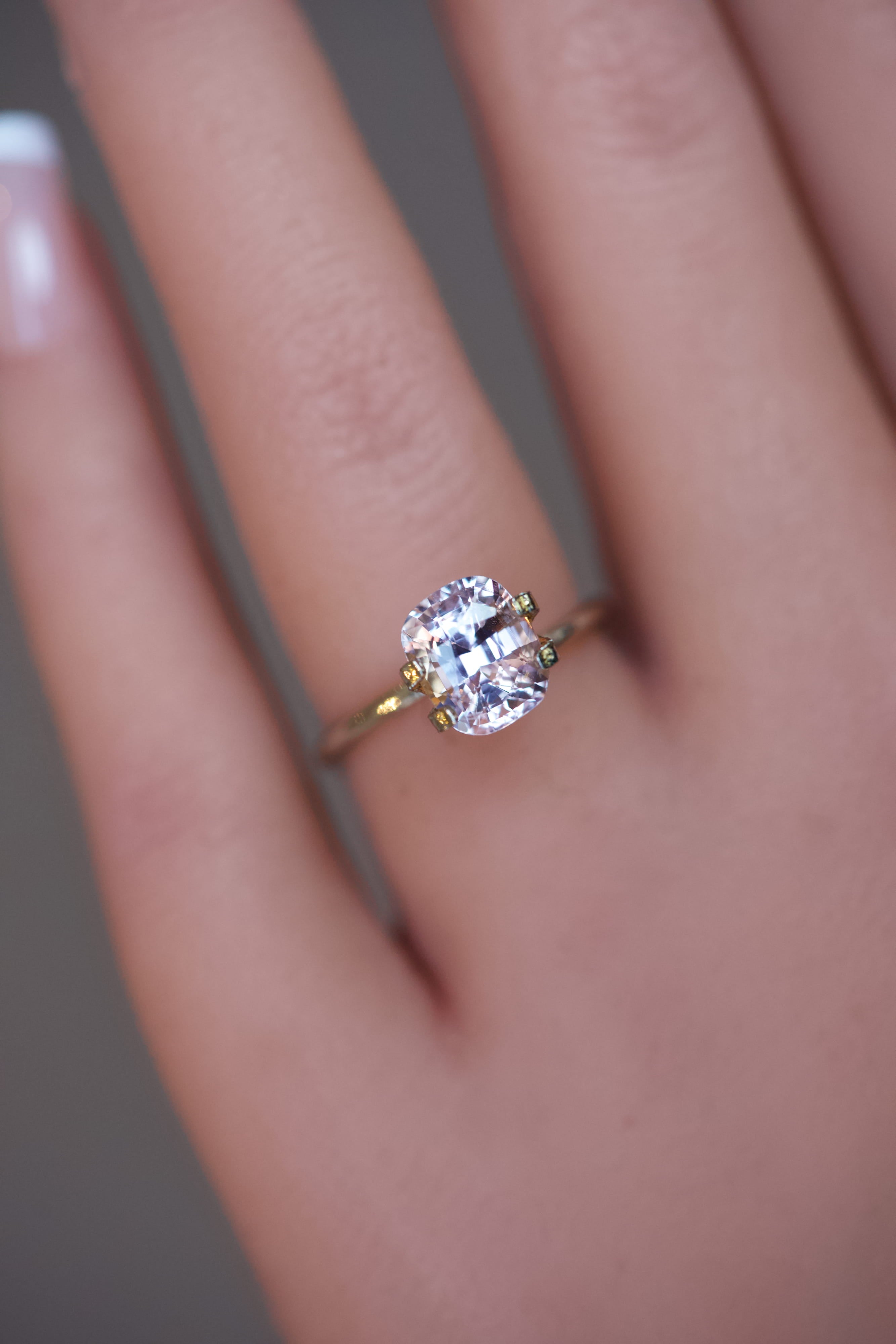 Detailed view of a soft pink Ceylon sapphire with a cushion cut, resting in a temporary ring setting.