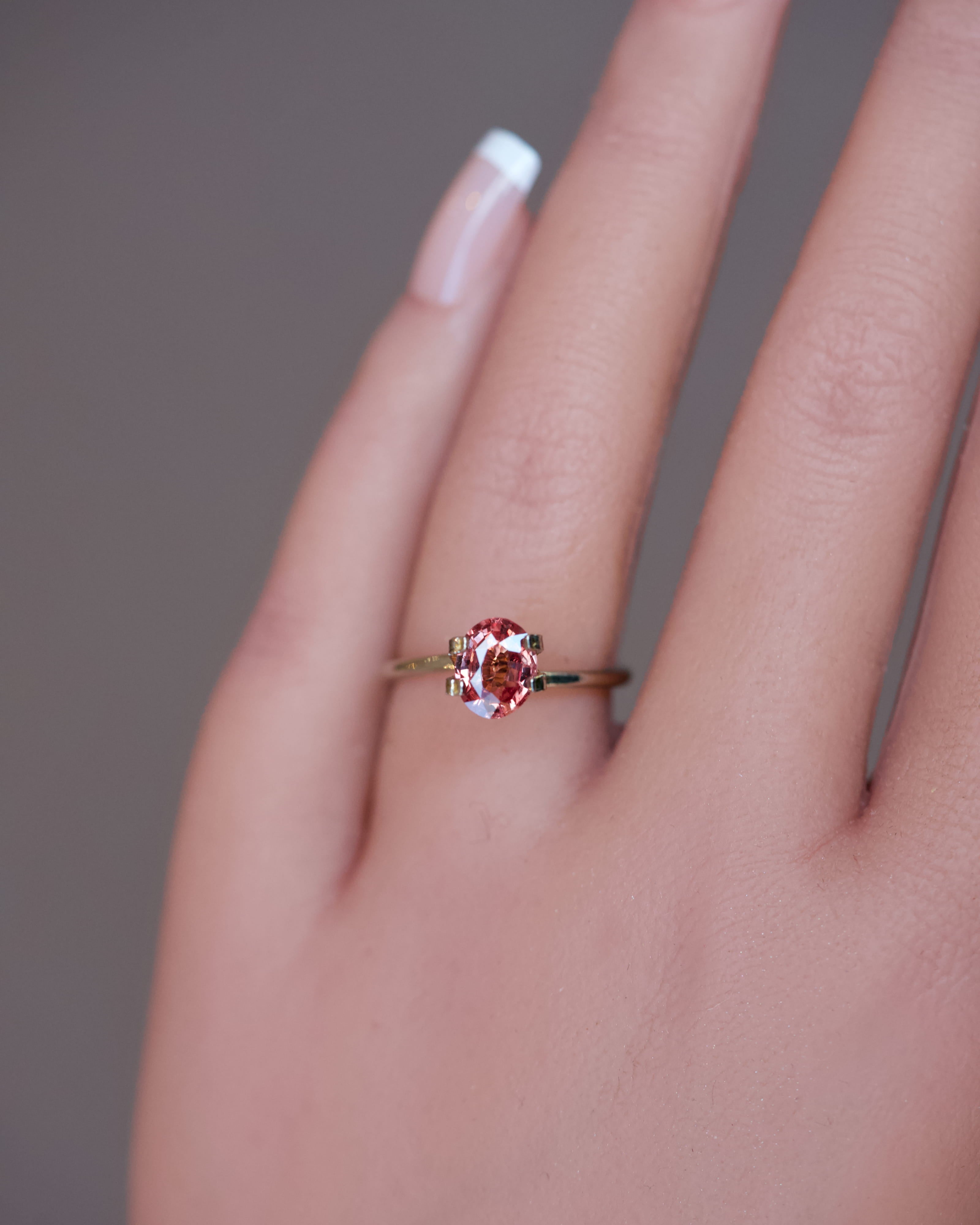 An unheated oval Padparadscha sapphire set in a temporary gold mock-up ring on a model's hand, showcasing its vibrant colour.