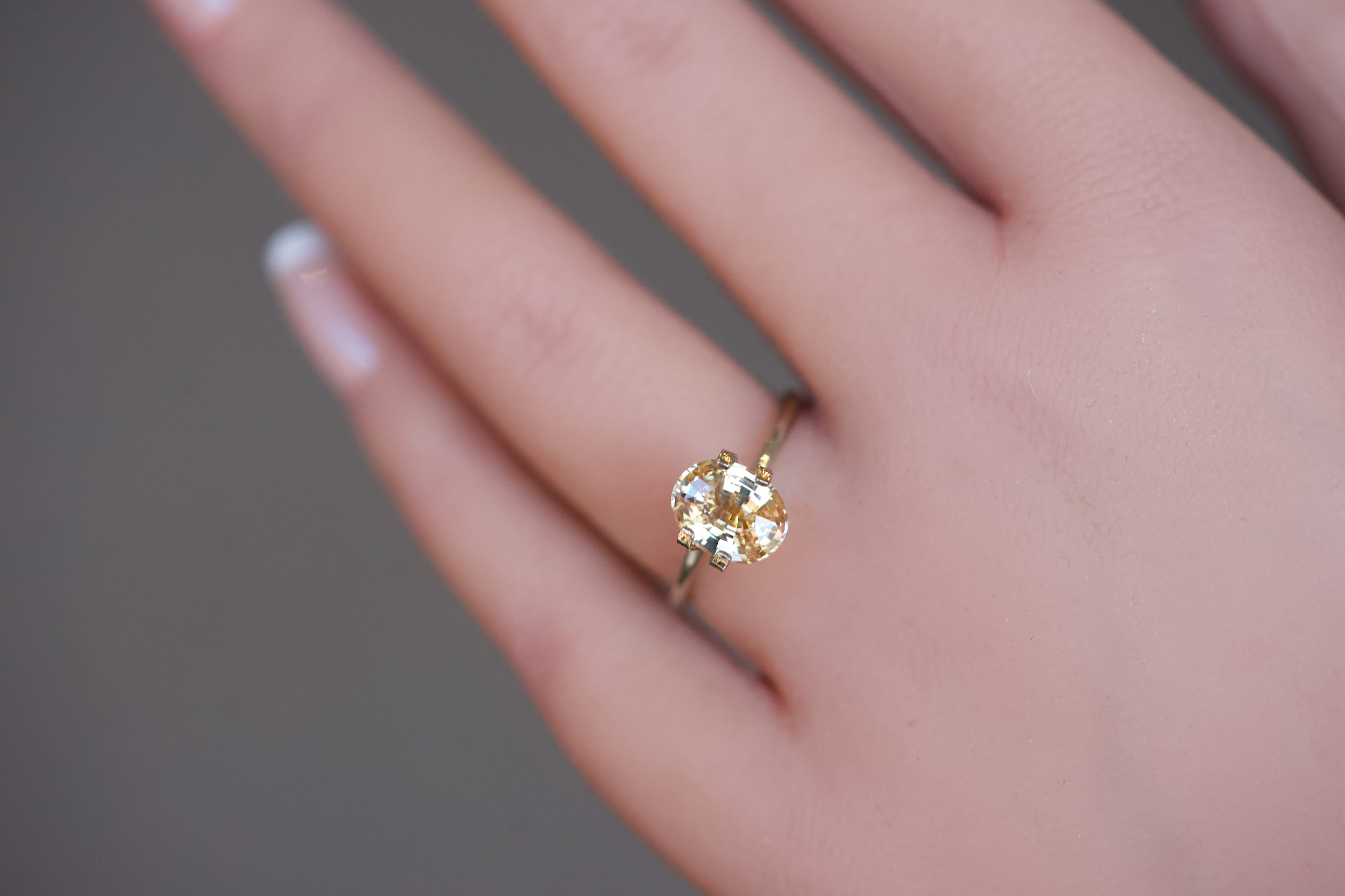 A vibrant, unheated orangy-yellow oval sapphire presented in a gold mock-up ring on a model's hand.