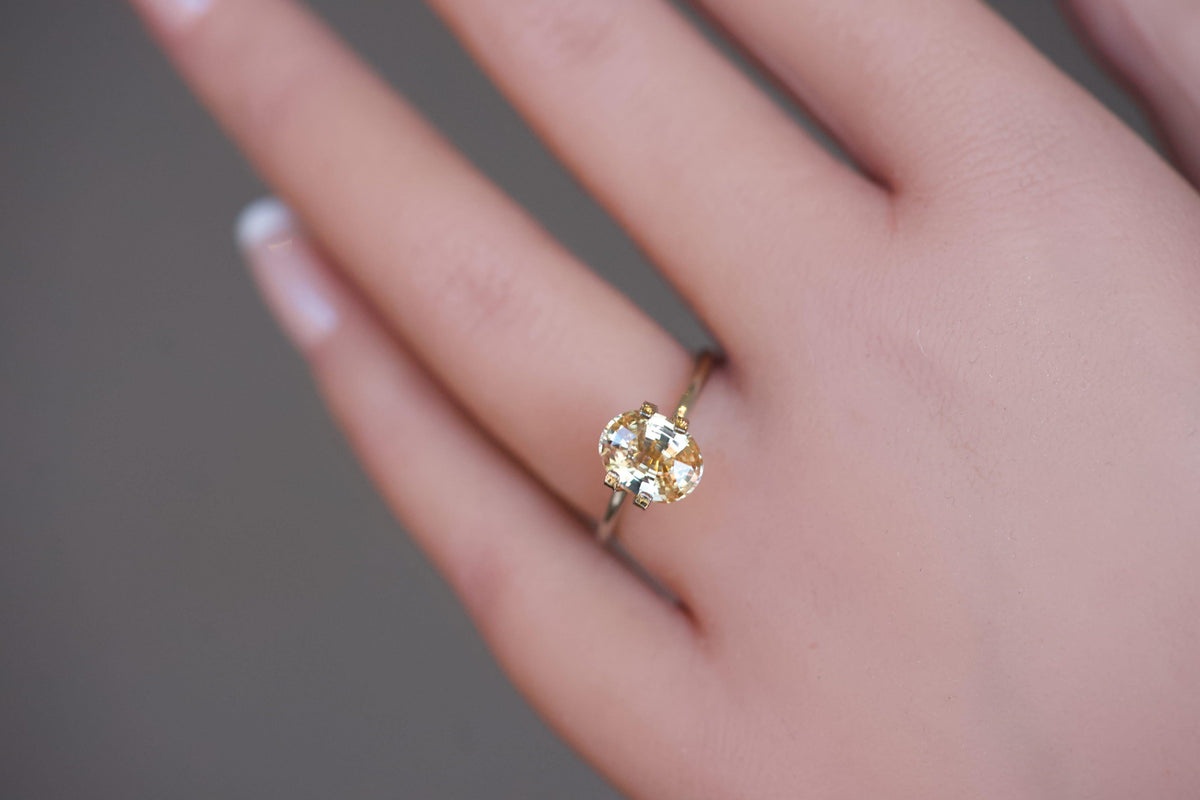 A vibrant, unheated orangy-yellow oval sapphire presented in a gold mock-up ring on a model's hand.
