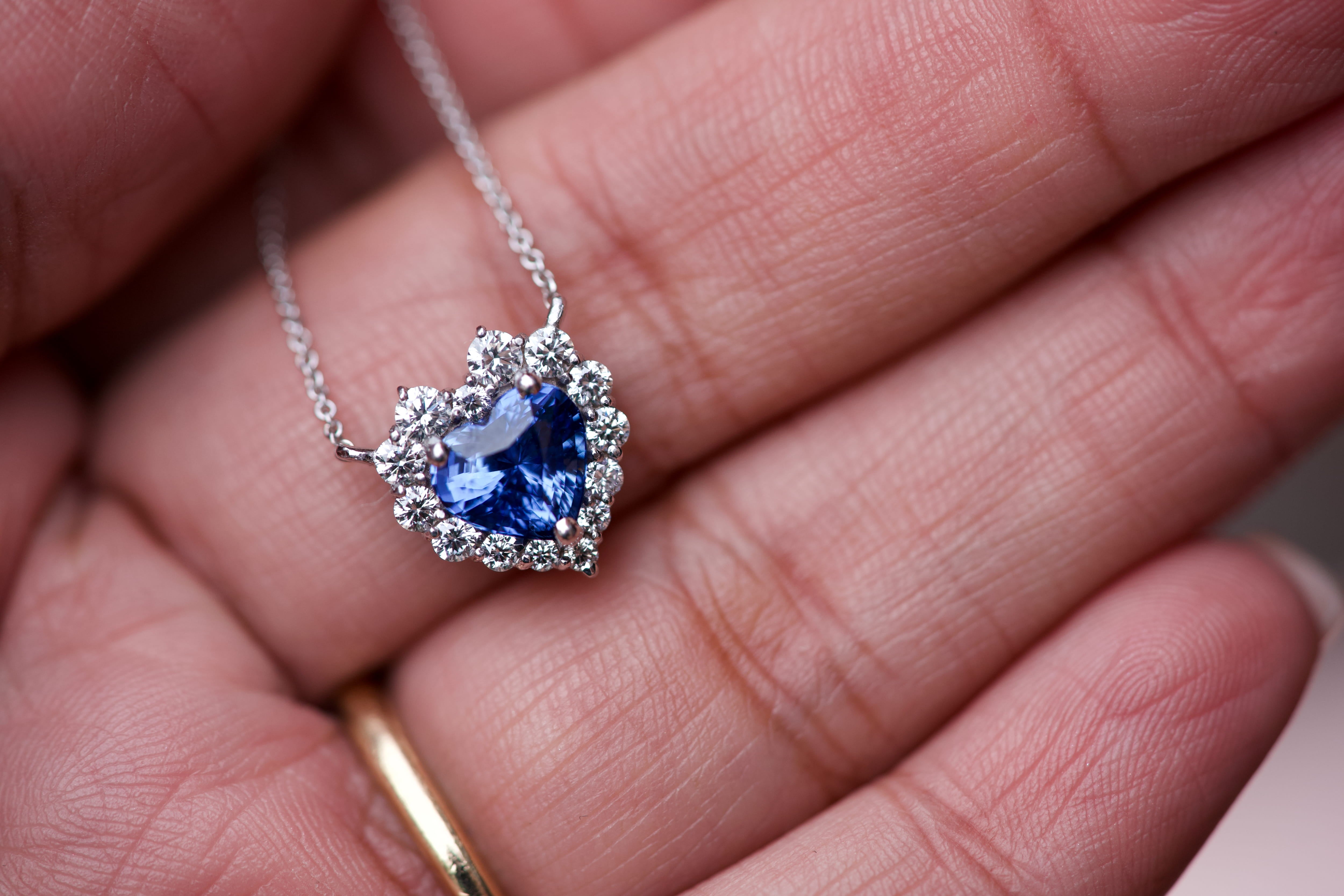 Vivid cornflower blue sapphire heart pendant with a graduated diamond halo resting on a hand