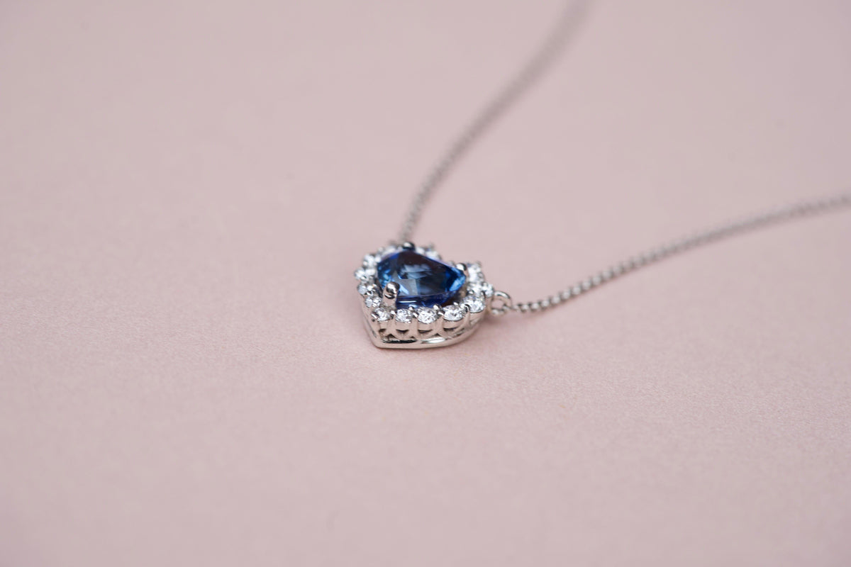 Side profile detail of the 18k white gold basket setting on a blue sapphire heart pendant