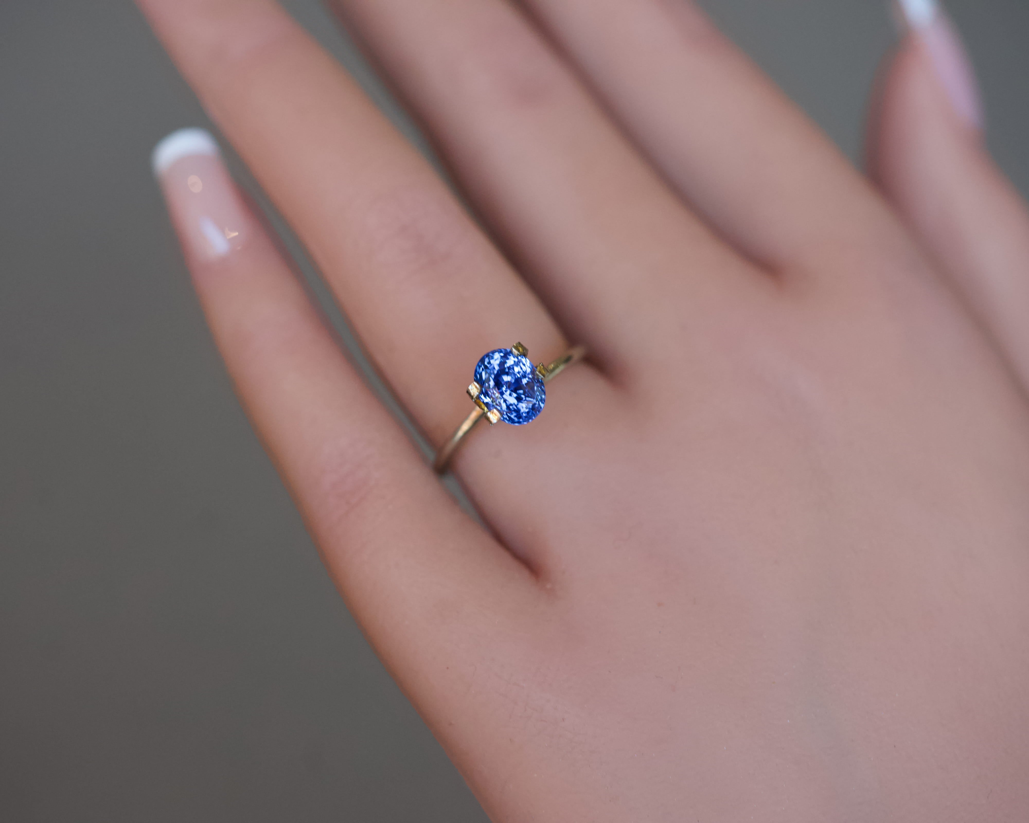 An unheated, natural blue-violet oval sapphire presented in a gold mock-up ring on a model's hand.