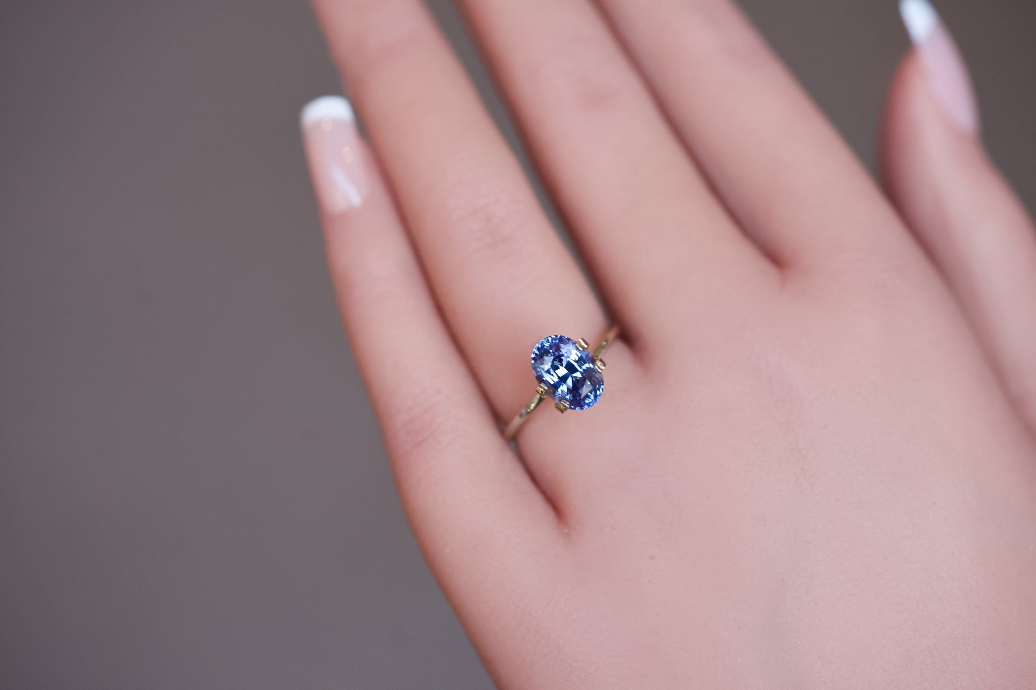An elegant, unheated bluish-violet oval sapphire set in a temporary gold ring on a hand.