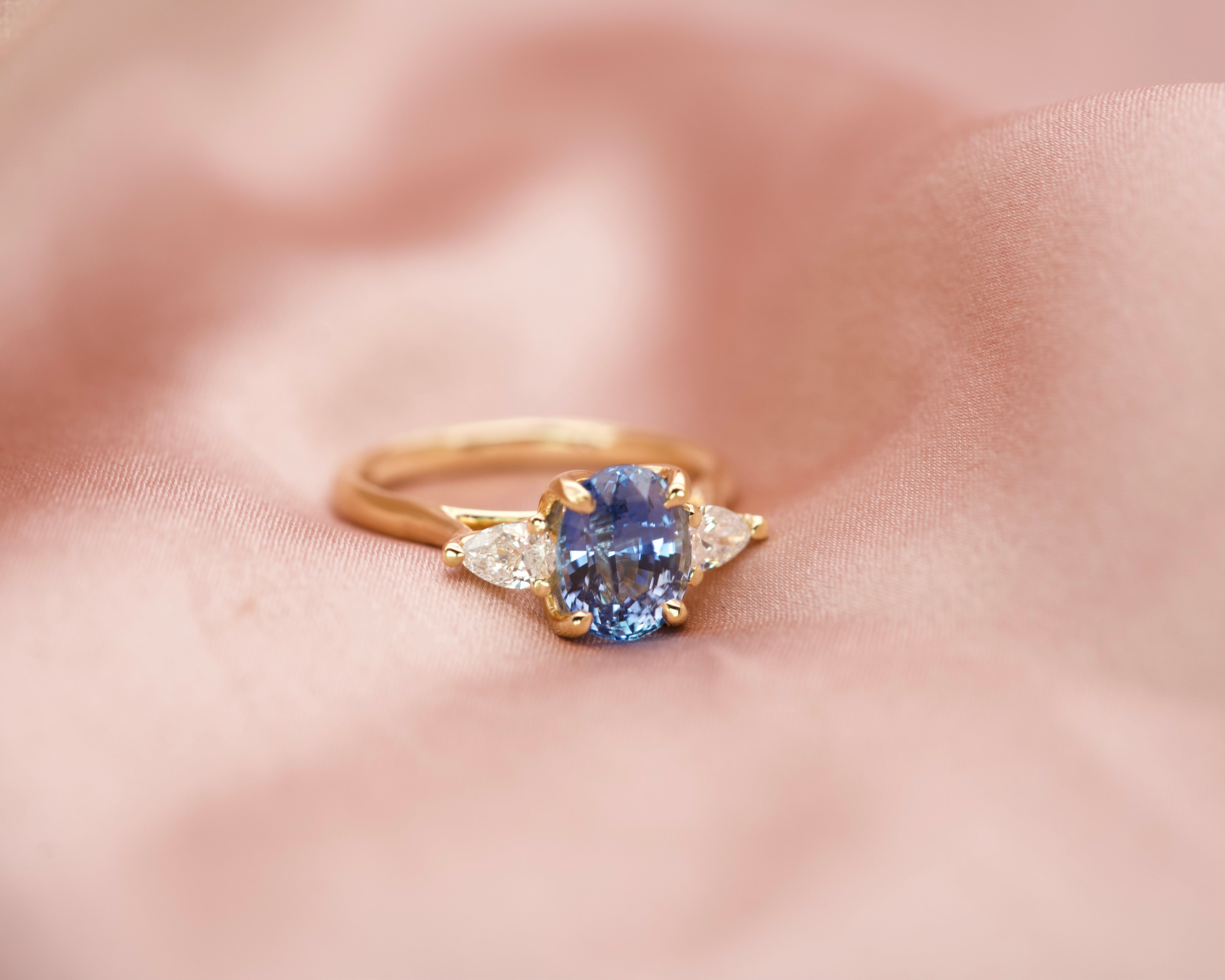 Top-down view of a medium blue oval sapphire flanked by two pear-cut diamonds in yellow gold