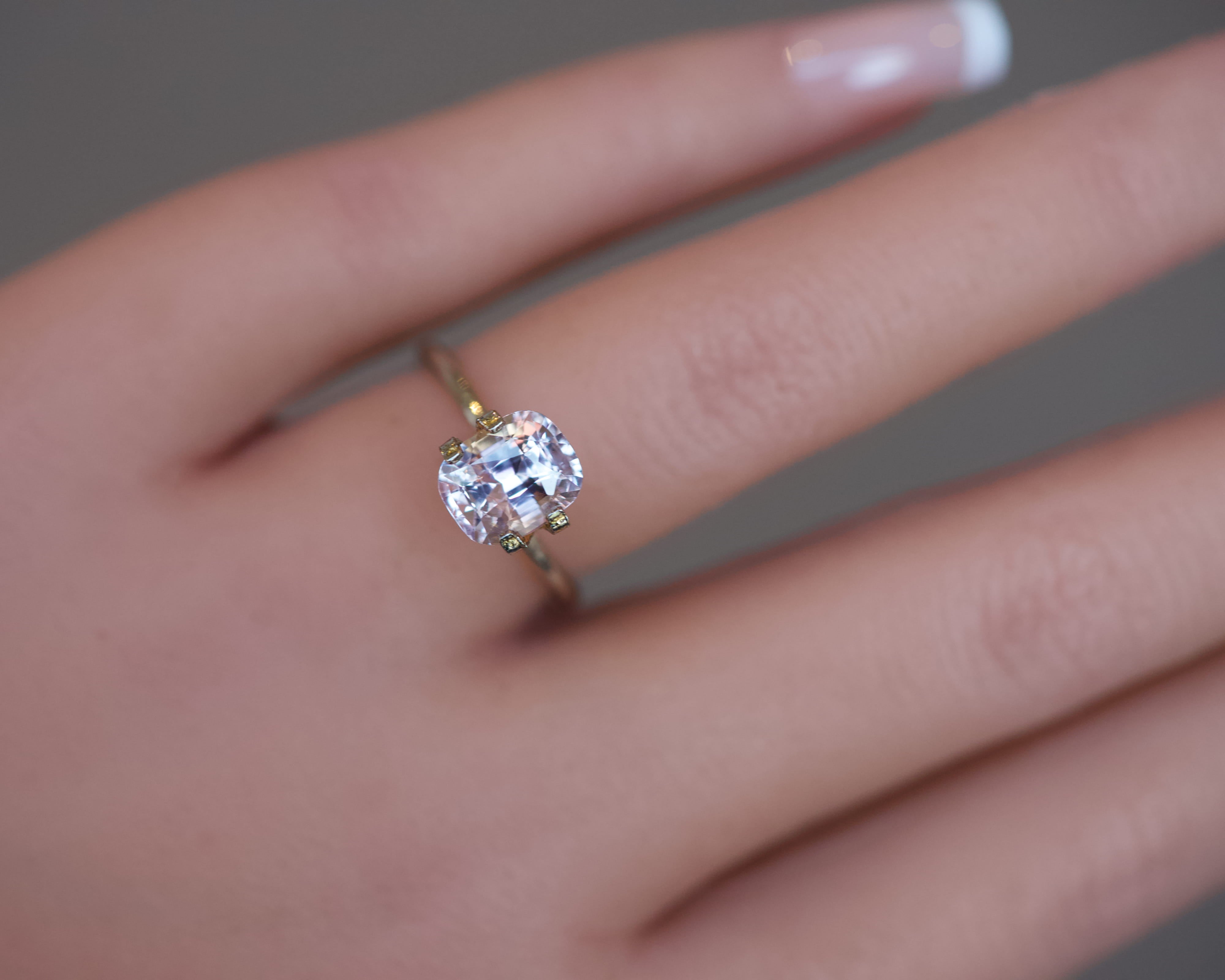 An elegant, unheated light pink cushion sapphire presented in a gold mock-up ring on a model's hand.