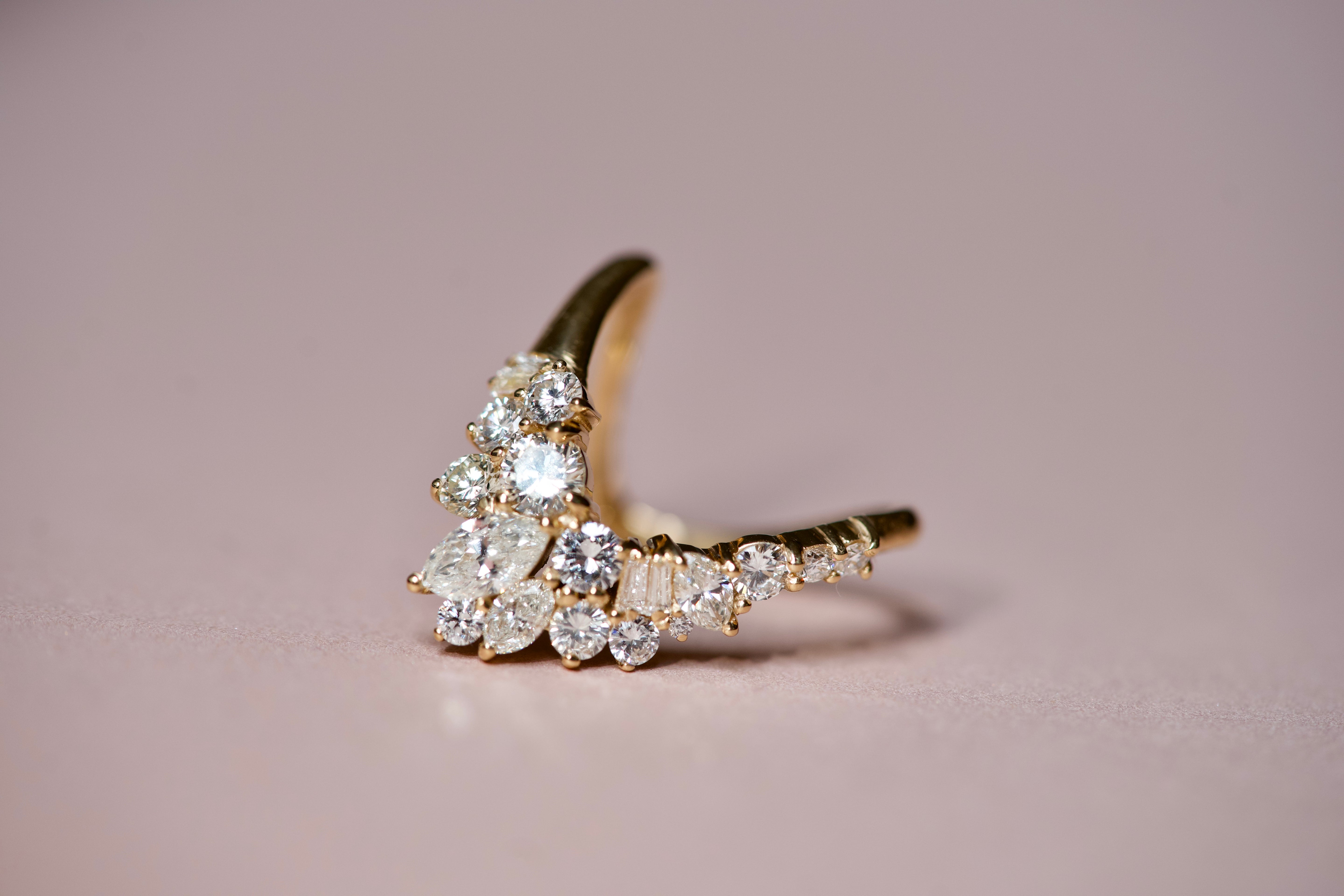 Luxury curved diamond cluster wedding band with marquise and round diamonds on a soft pink background