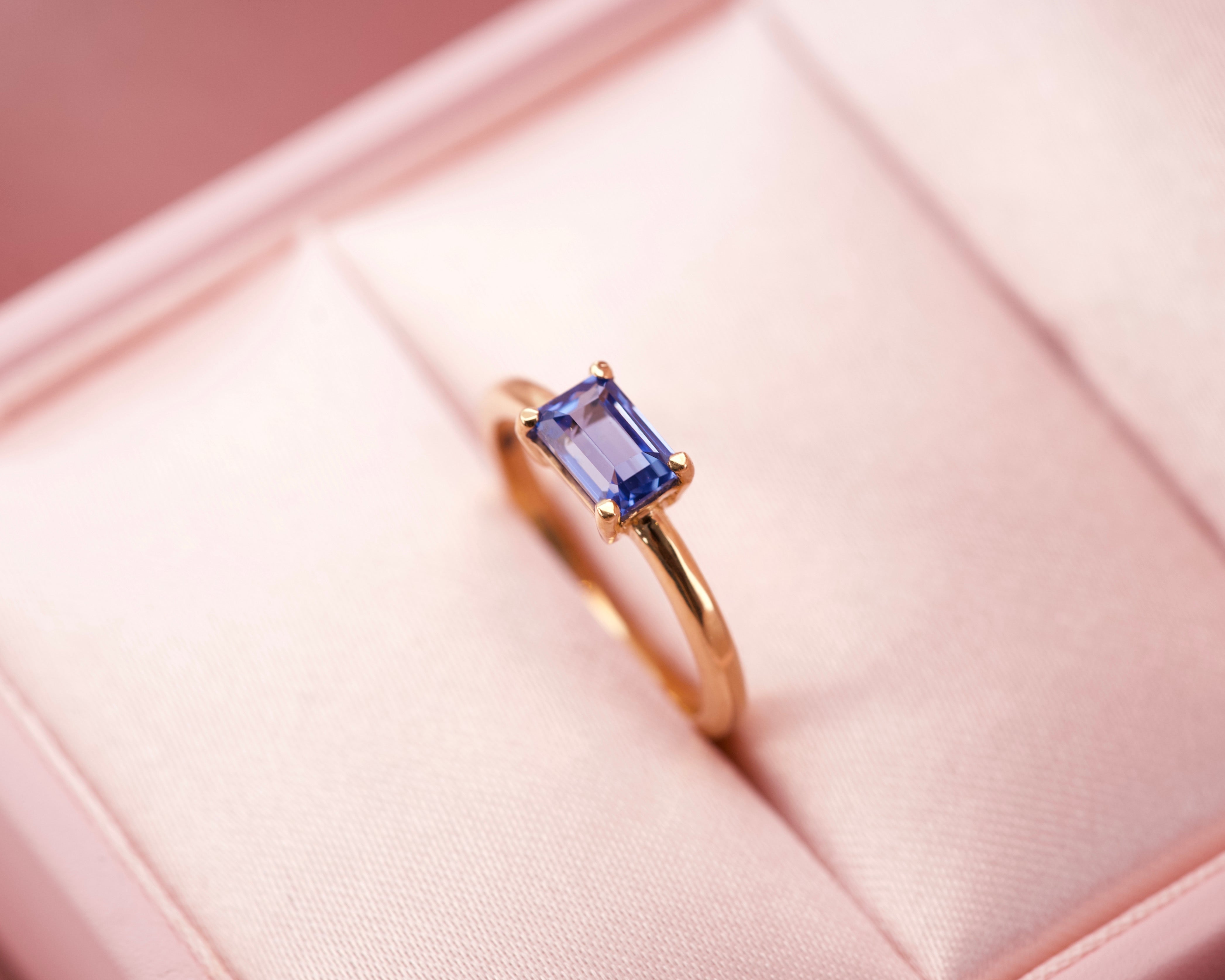 A vivid cornflower blue emerald cut sapphire set horizontally in an 18k yellow gold solitaire ring