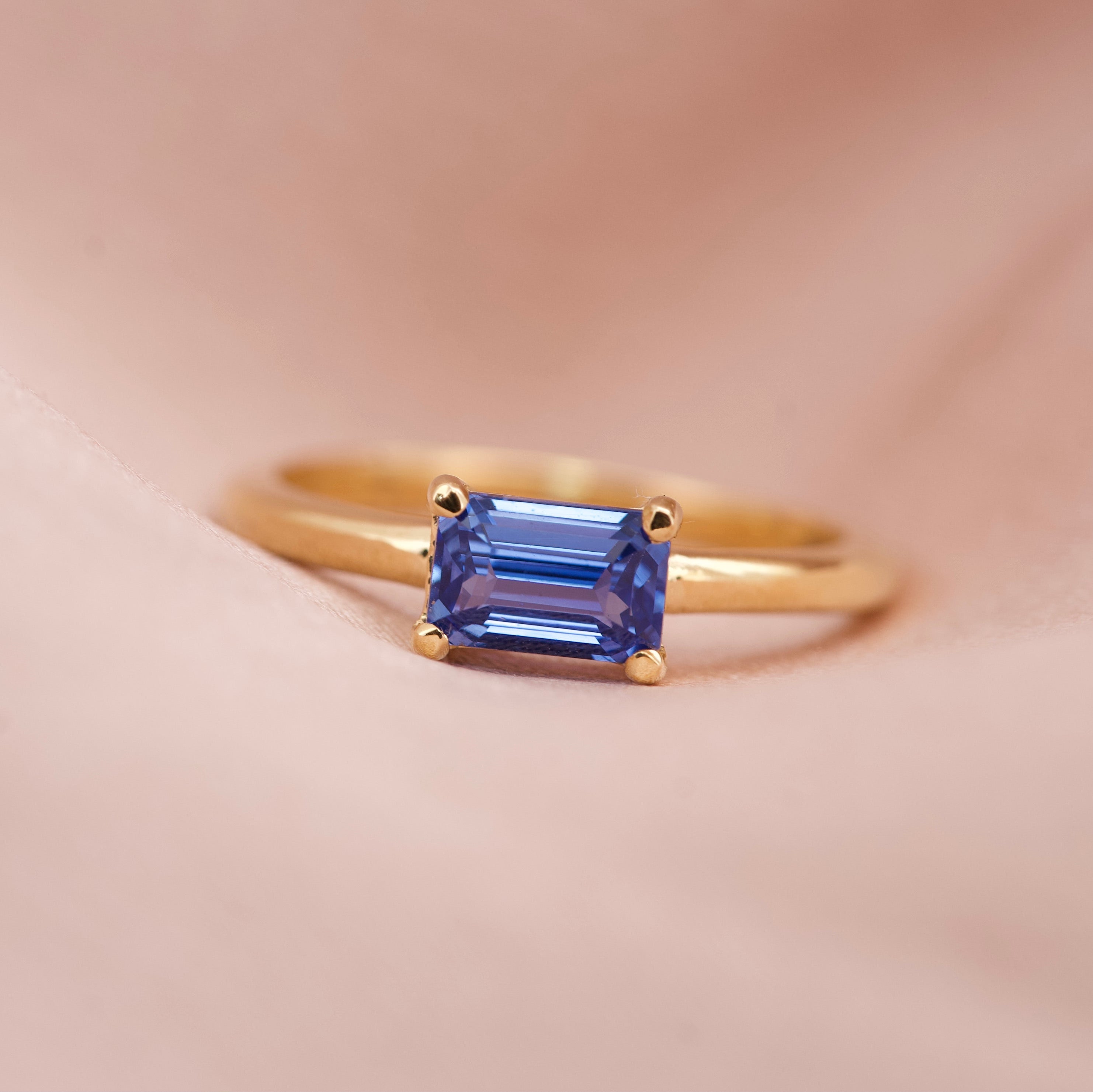 A vivid cornflower blue emerald cut sapphire set horizontally in an 18k yellow gold solitaire ring
