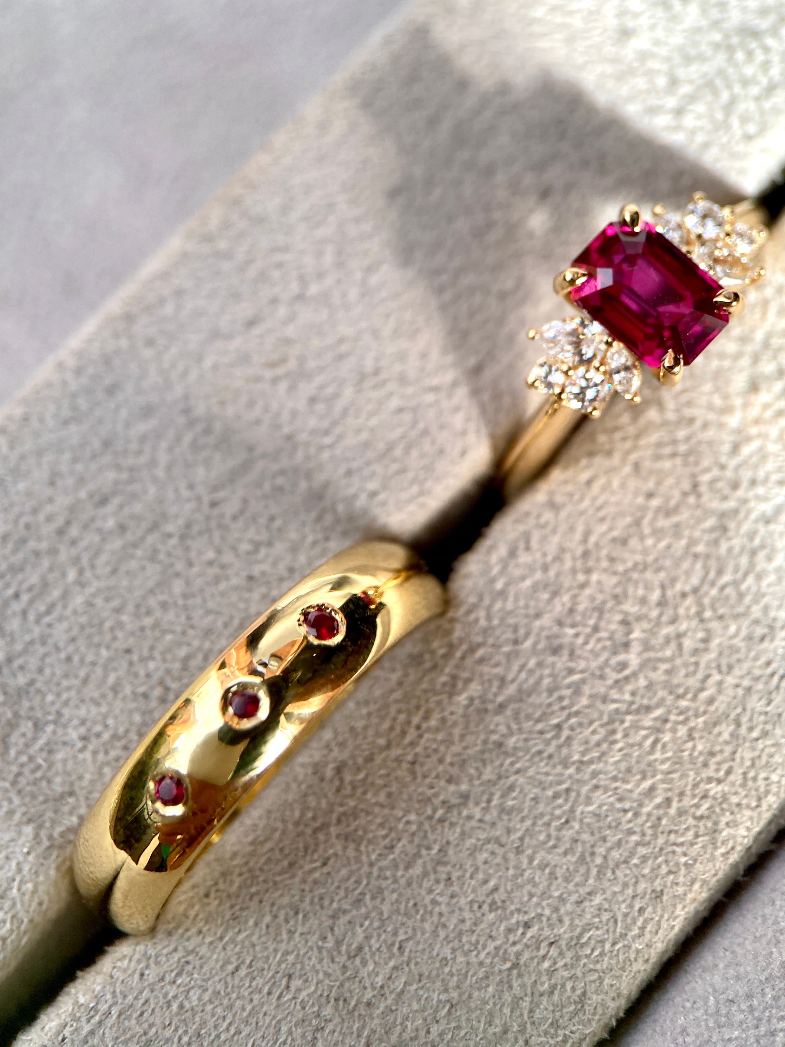 Luxury emerald cut ruby engagement ring alongside a wide yellow gold wedding band flush-set with round rubies