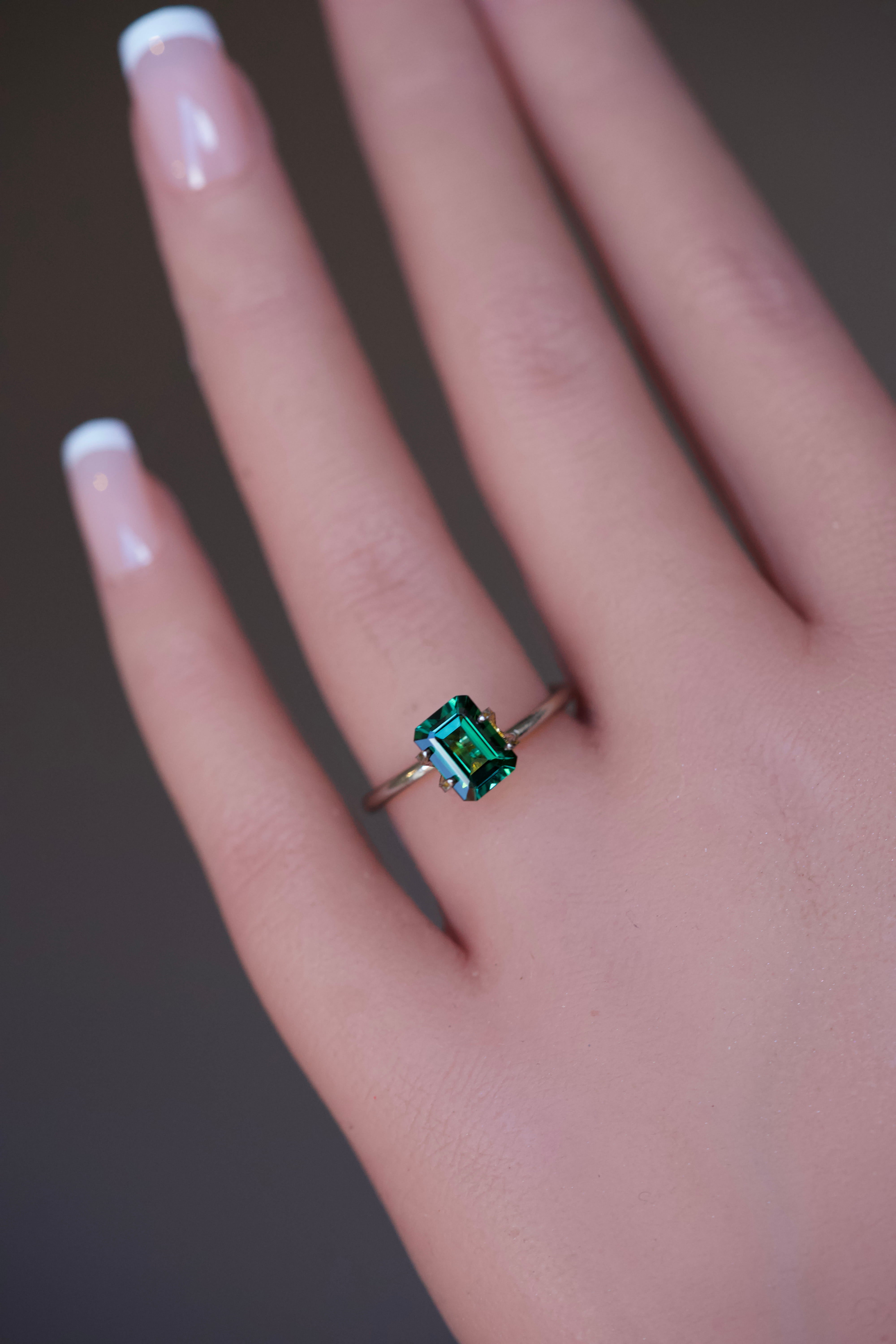 A 1.63 carat green rectangular step-cut Tourmaline displayed in a temporary gold ring setting on a hand.