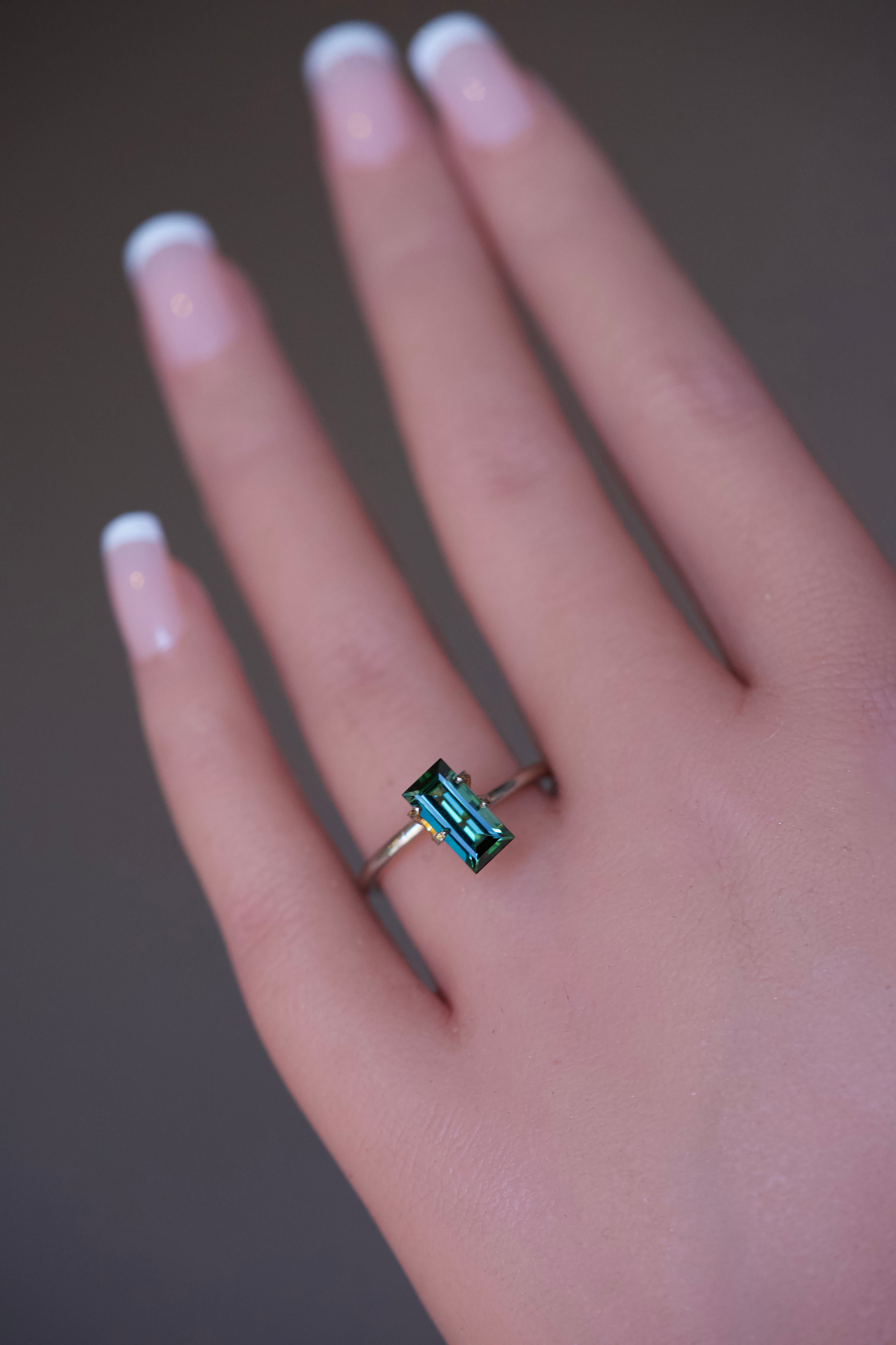 Rectangular step-cut green Tourmaline in a gold ring mockup on a hand.