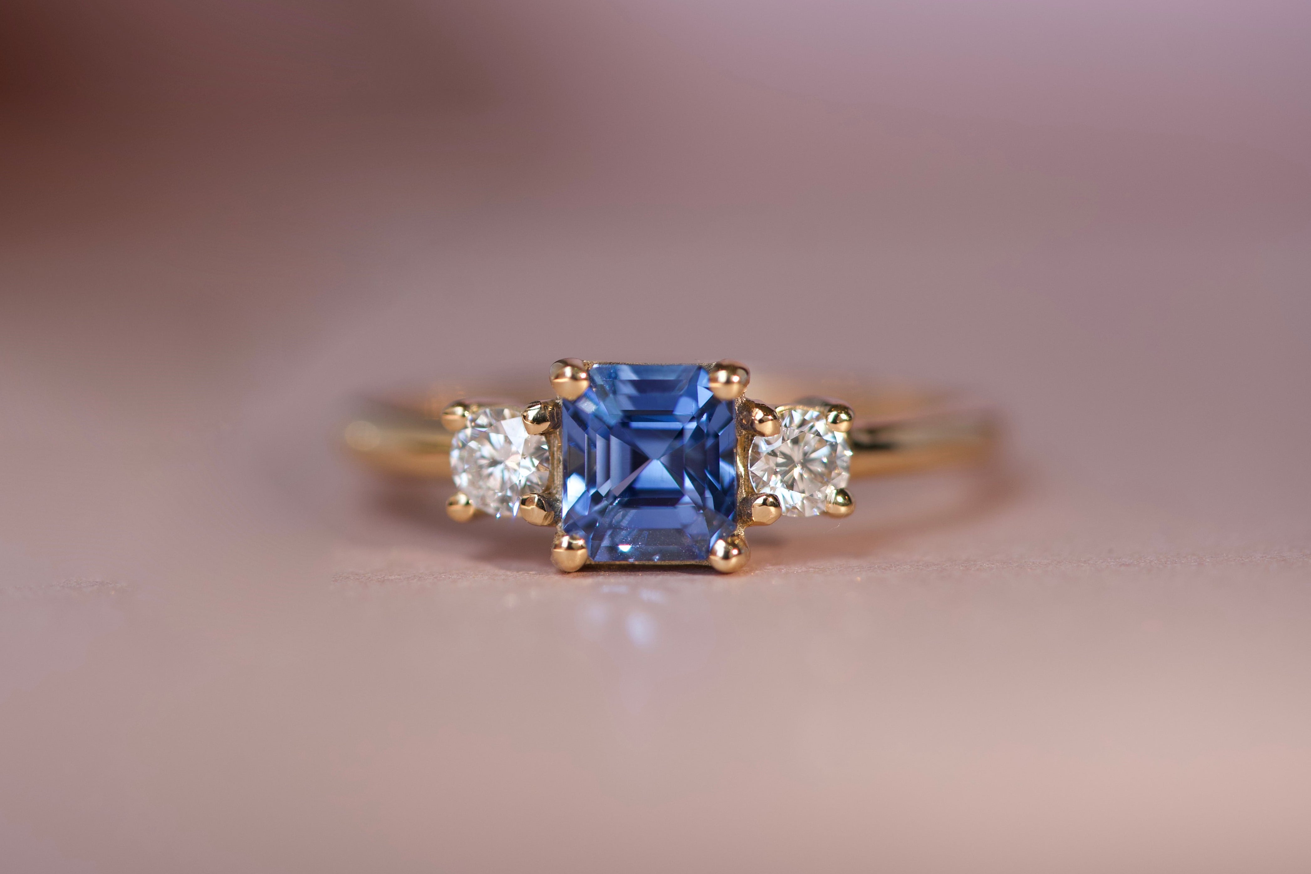Handcrafted Ceylon sapphire and diamond trilogy ring in 18k yellow gold with low profile setting, front view on neutral background