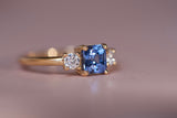 Side angle view of luxury blue sapphire trilogy engagement ring showing depth of setting and brilliant diamond accents in warm gold