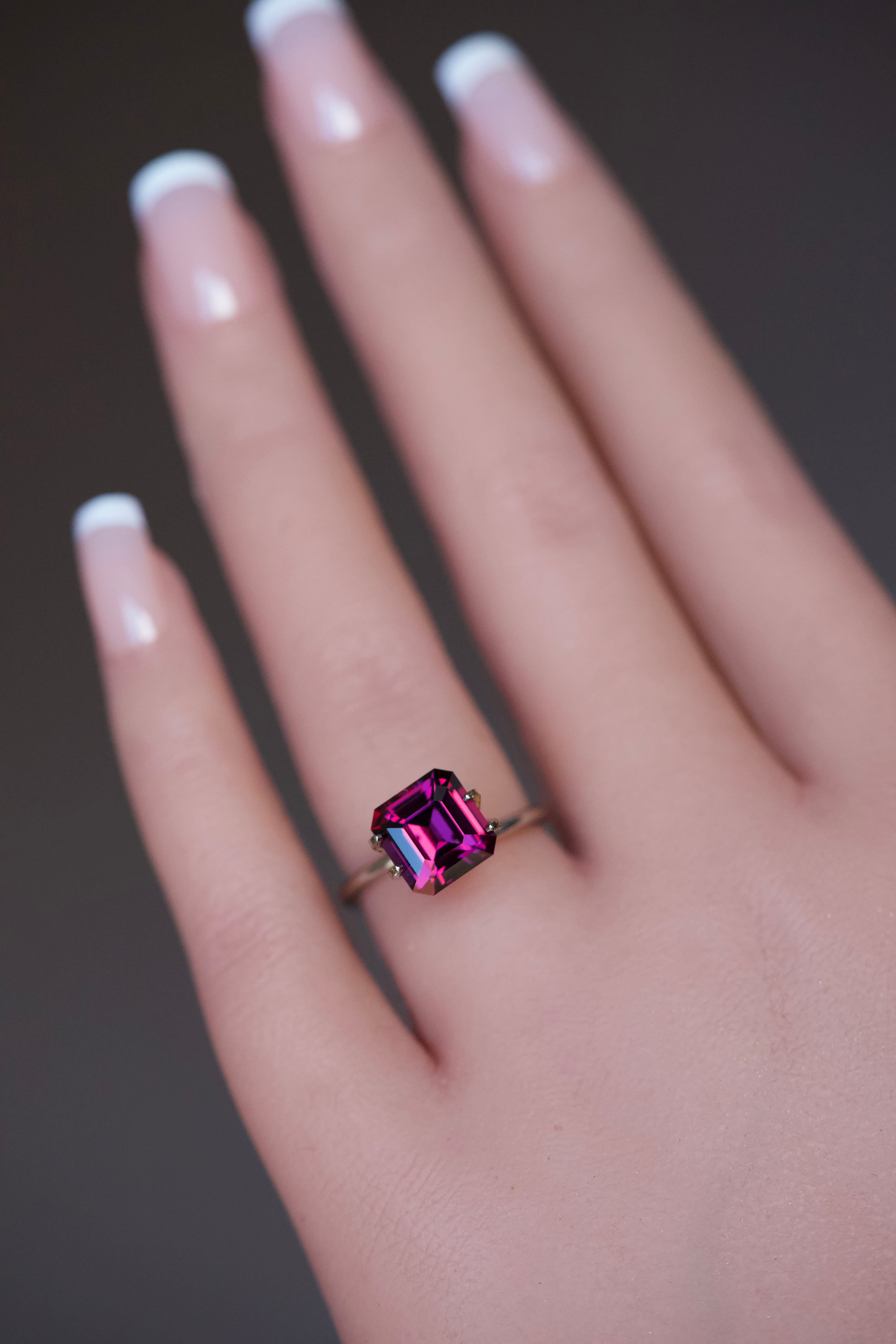 Orchid-toned rectangular step-cut garnet showcased on a model's finger.