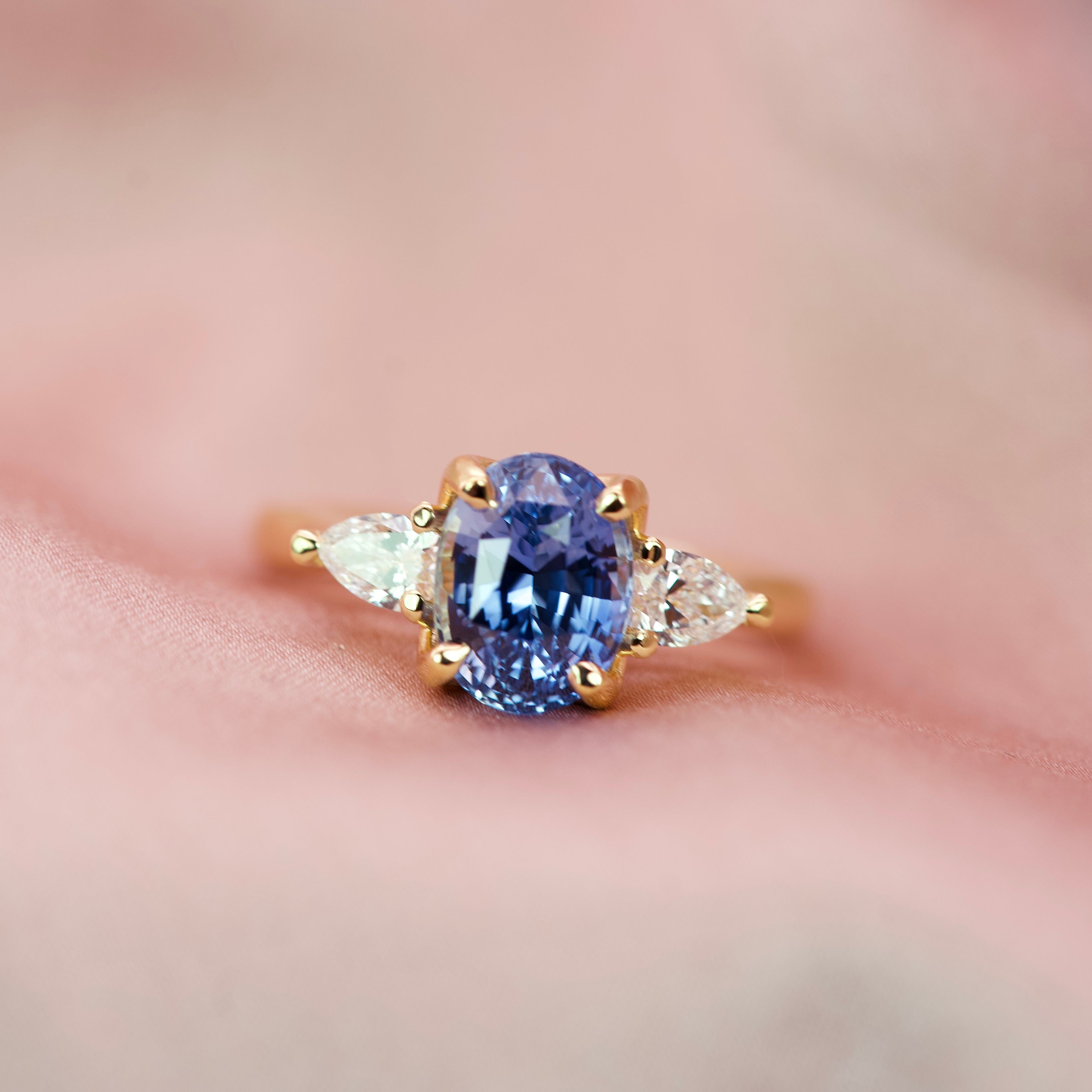 Top-down view of a medium blue oval sapphire flanked by two pear-cut diamonds in yellow gold