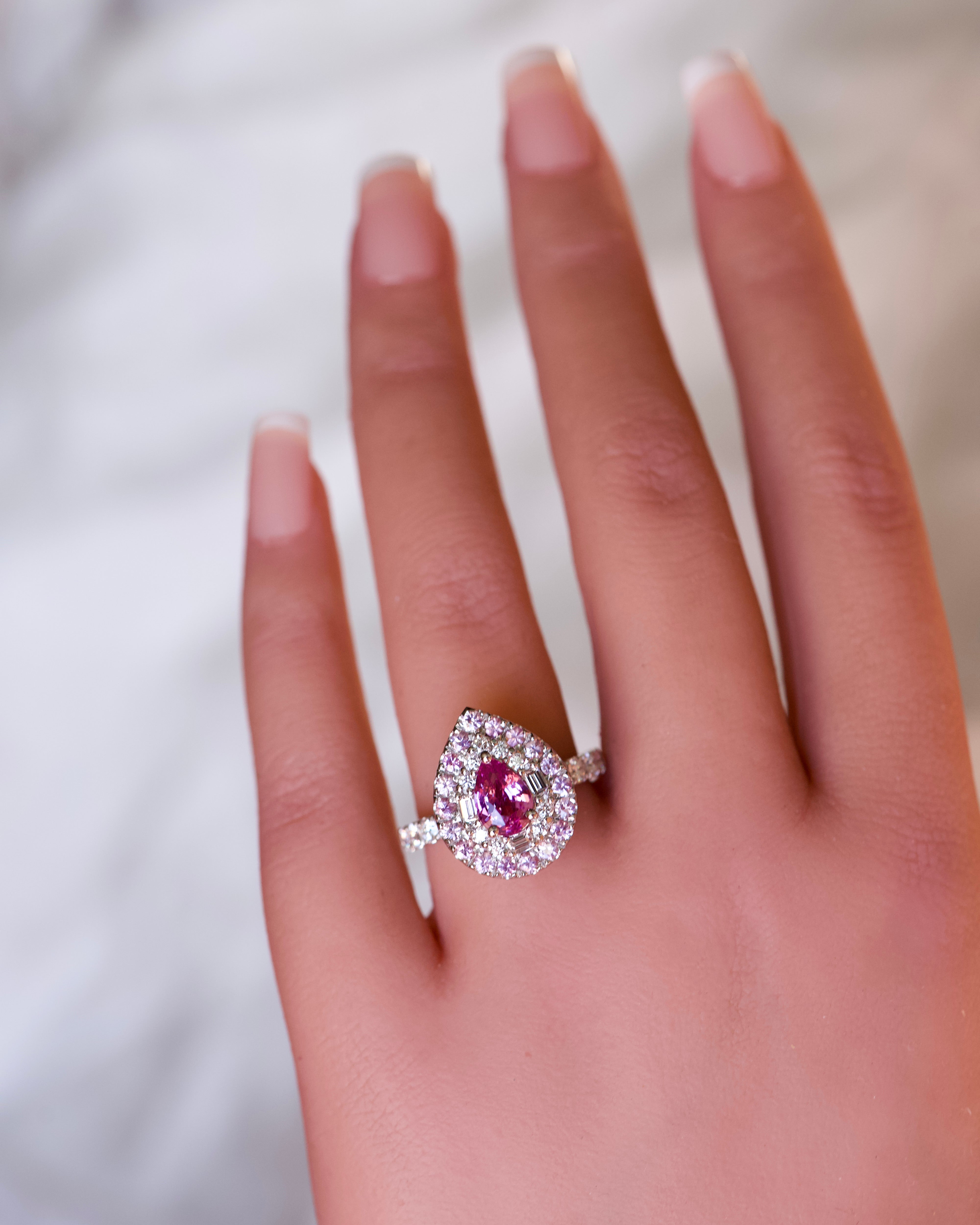 A luxury pear-shaped pink sapphire ring with a double halo worn on a hand