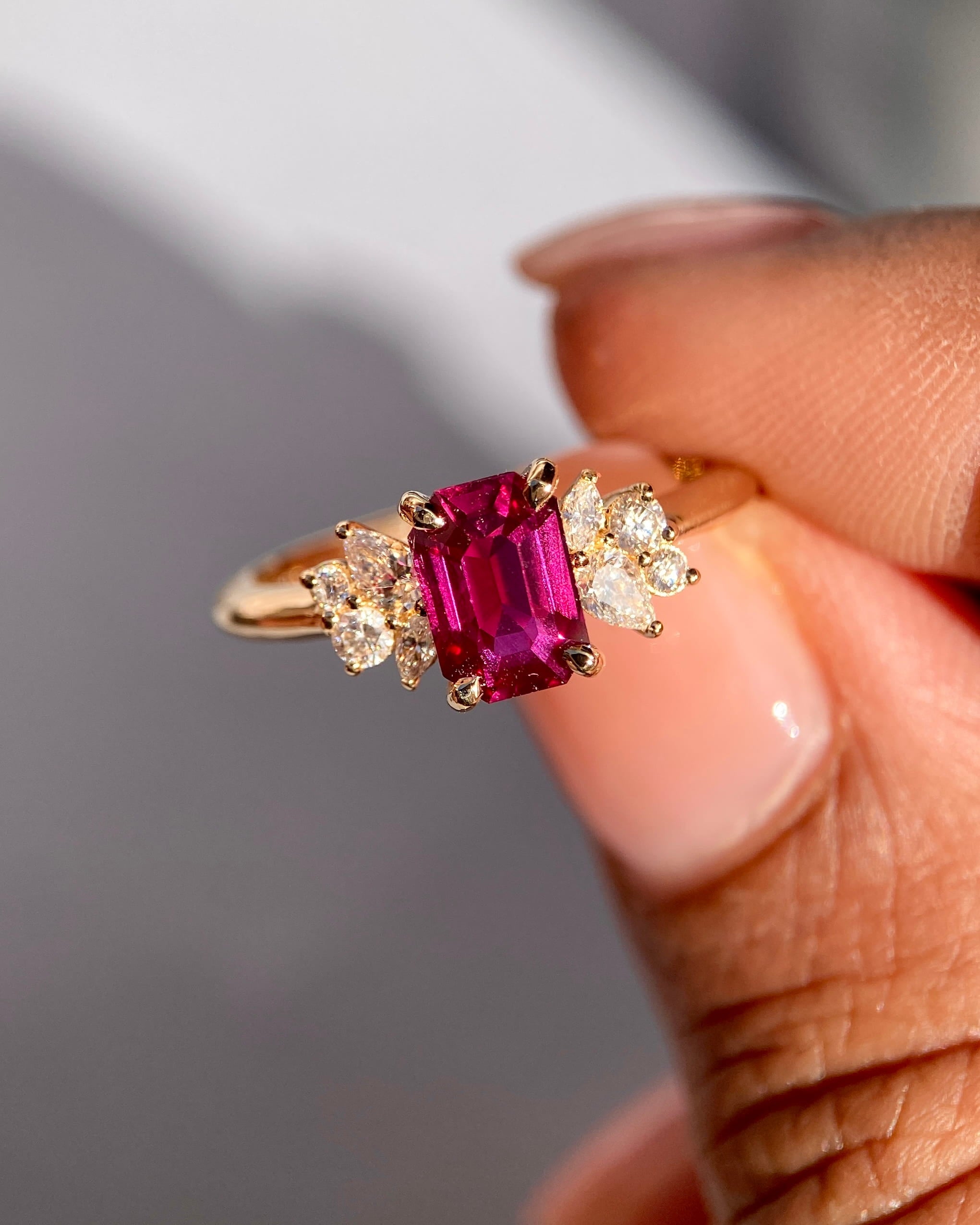 A 1.17ct emerald cut red ruby ring with sparkling side diamonds held between fingers