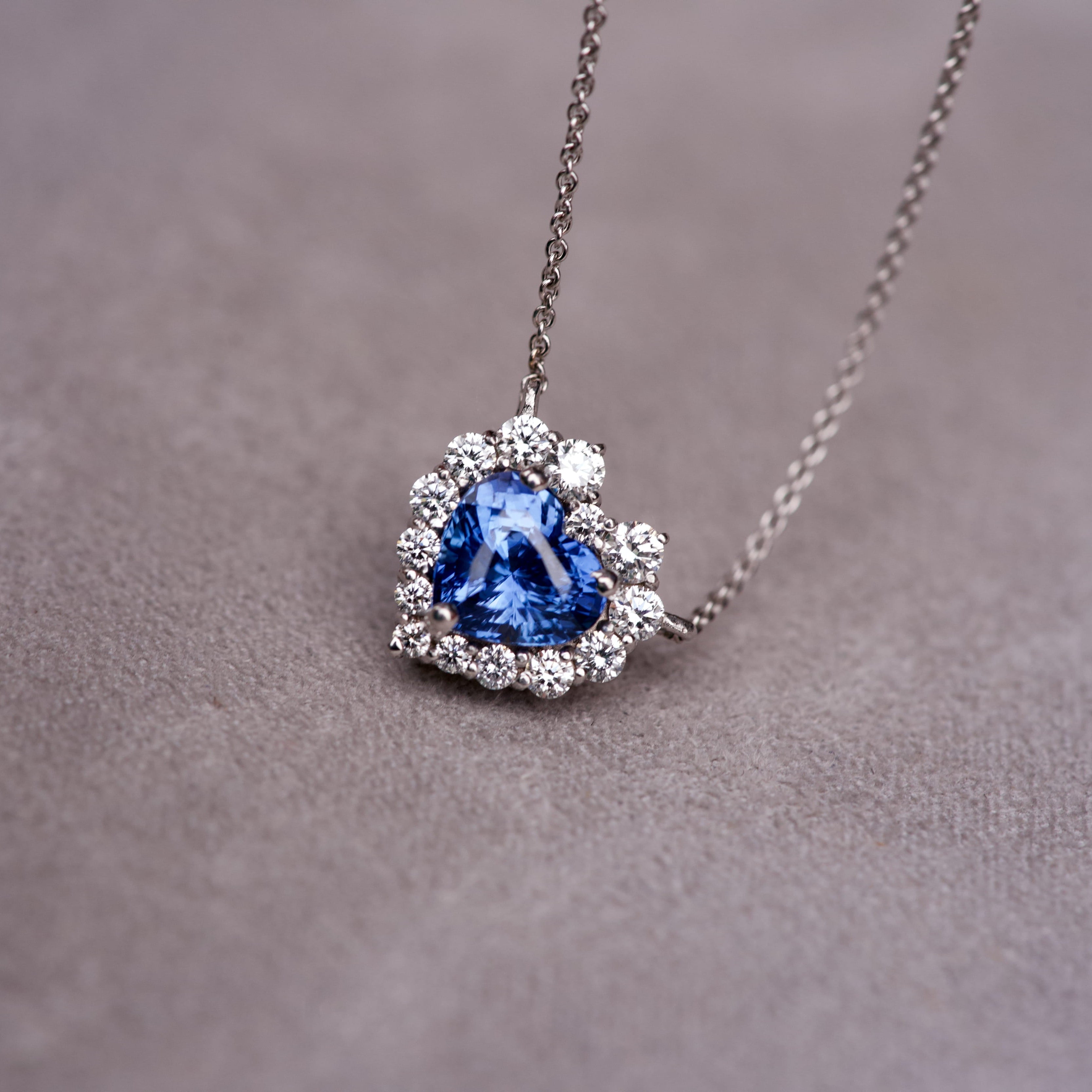Heart shaped blue sapphire pendant with a sparkling graduated diamond halo on a grey textured surface