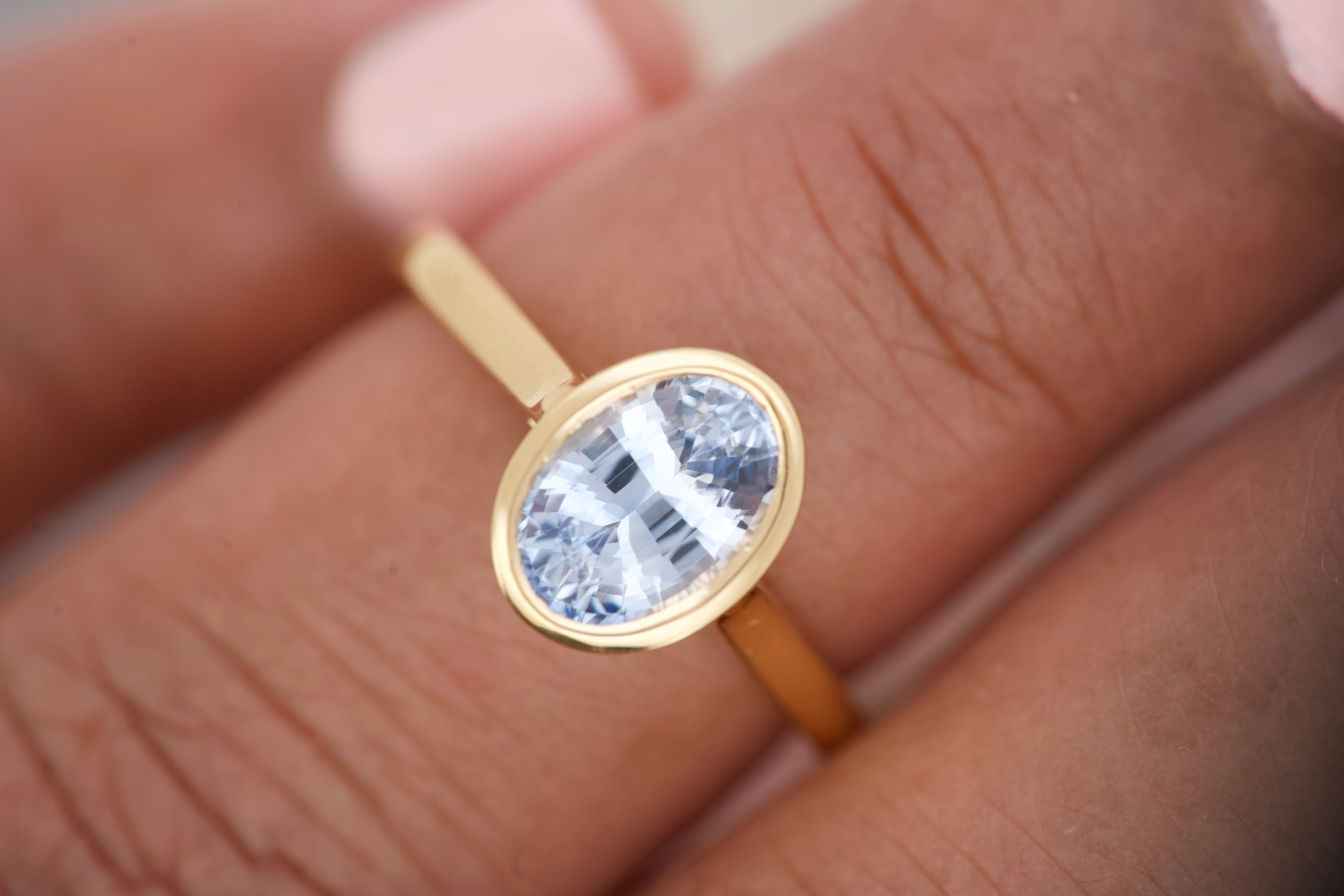 Oval blue sapphire bezel ring worn on hand, close-up