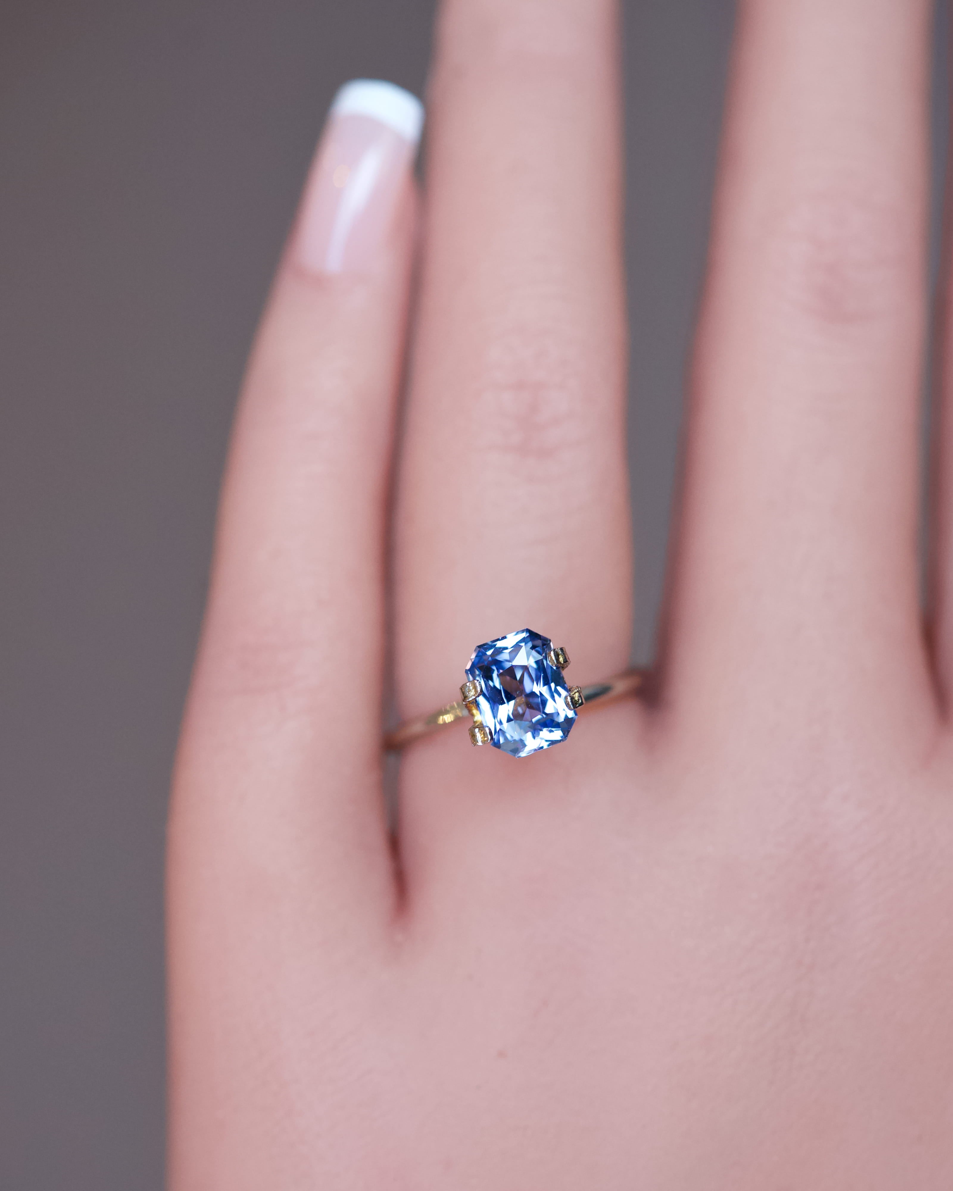 An unheated blue octagonal sapphire displayed in a gold mock-up ring on a hand.