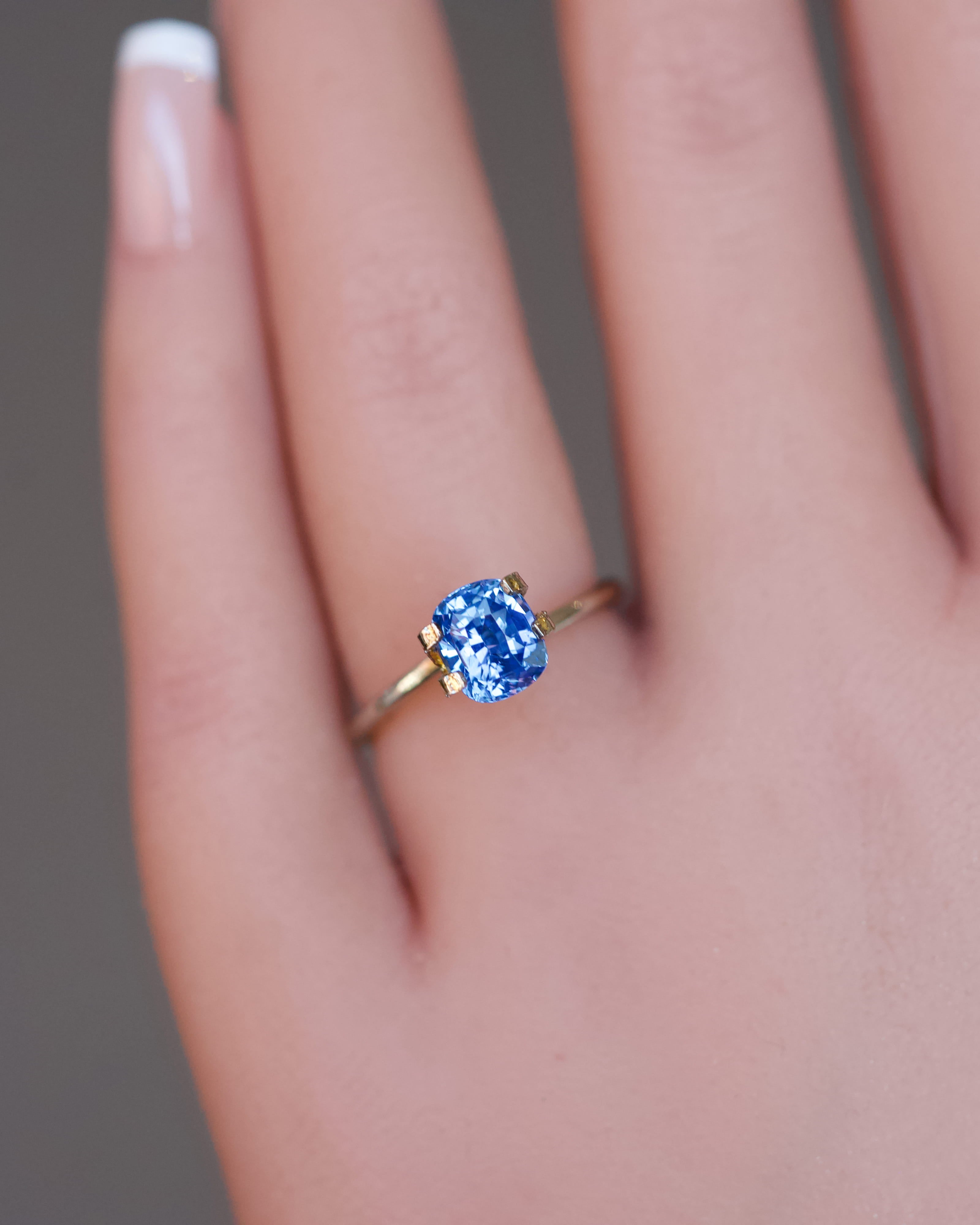 An unheated blue cushion sapphire presented in a gold ring setting on a model's hand.