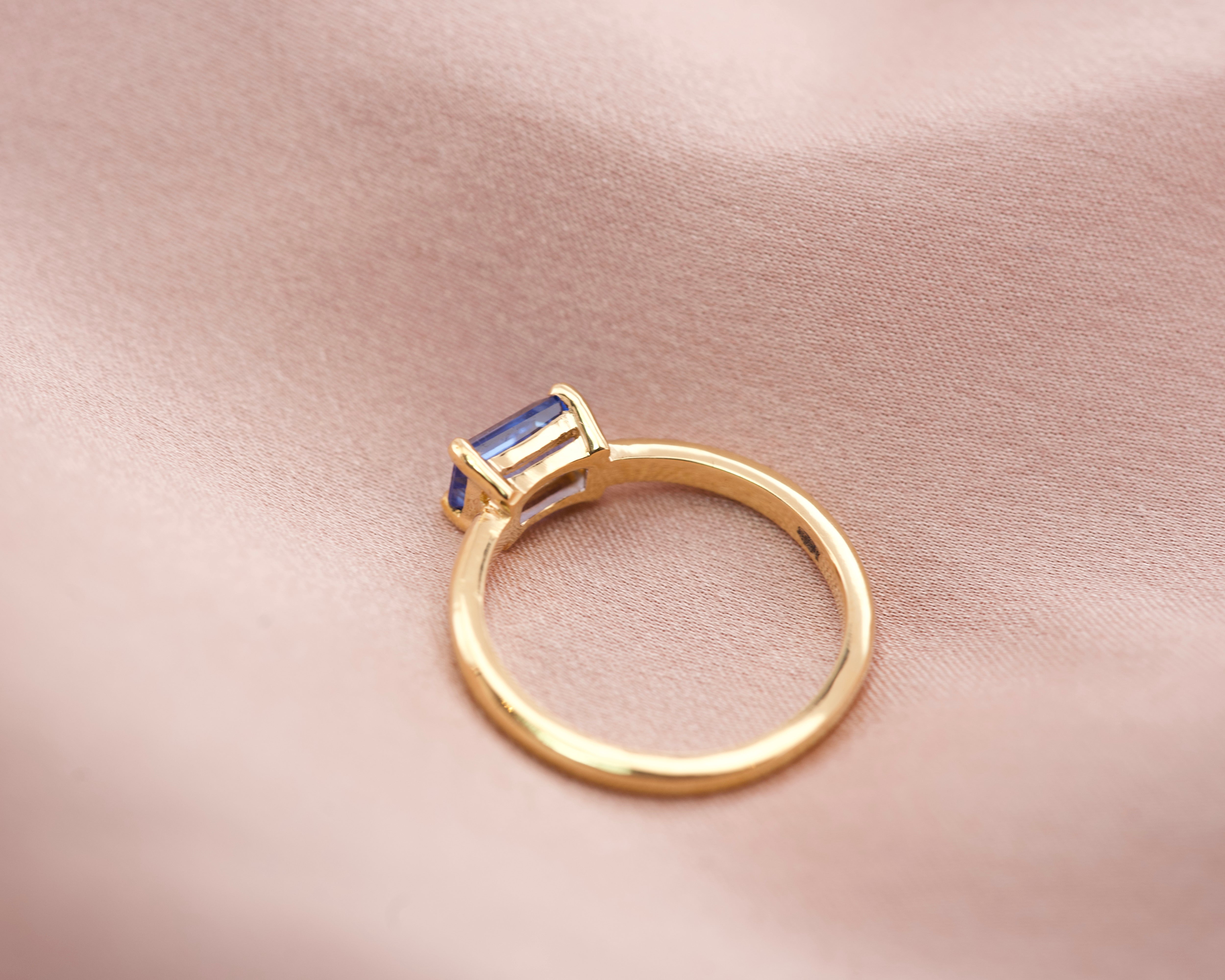 Side view of a low profile emerald cut blue sapphire ring showing the 18k yellow gold band