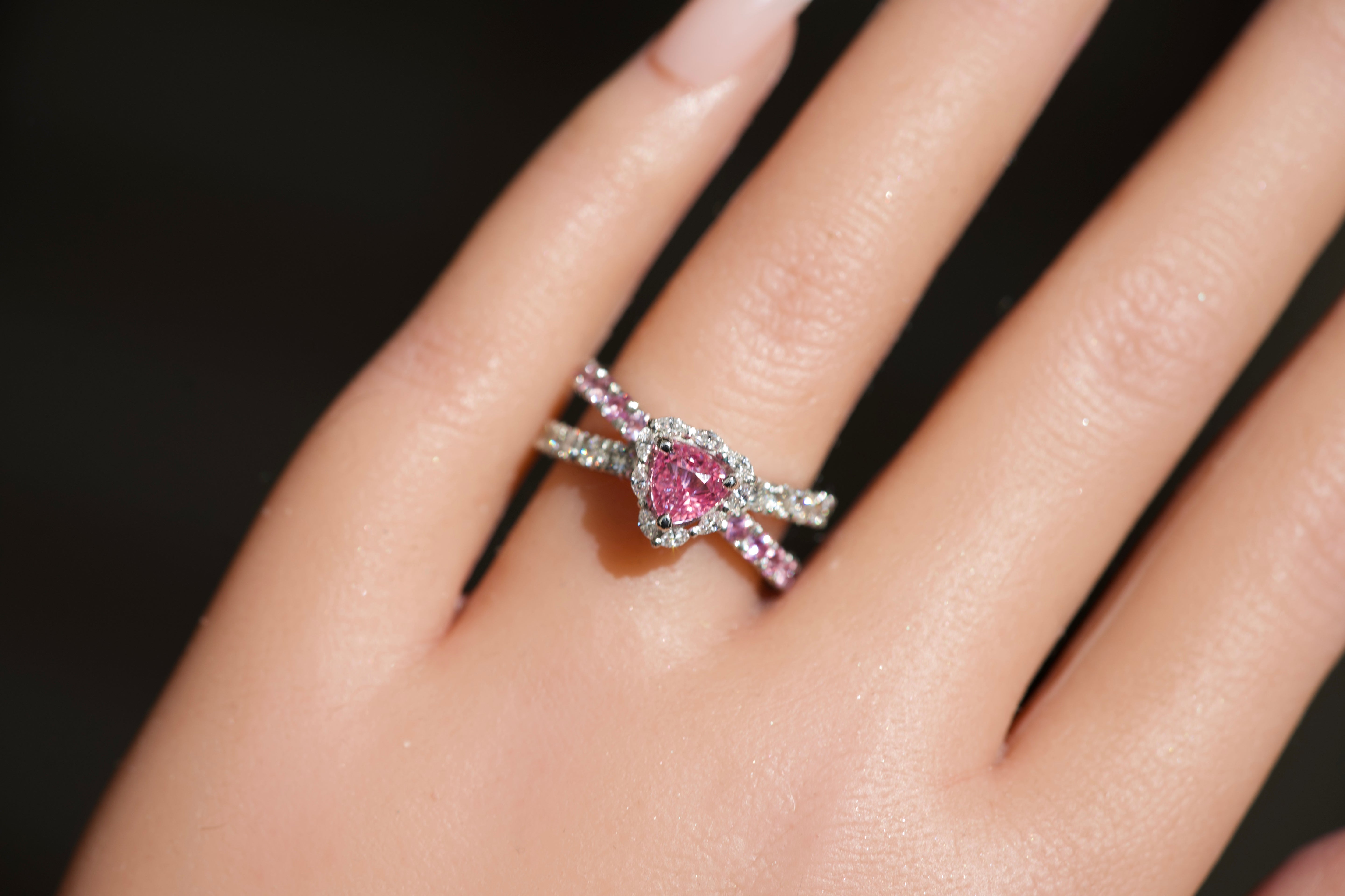 Vivid pink sapphire engagement ring worn on a hand showing the split pavé band