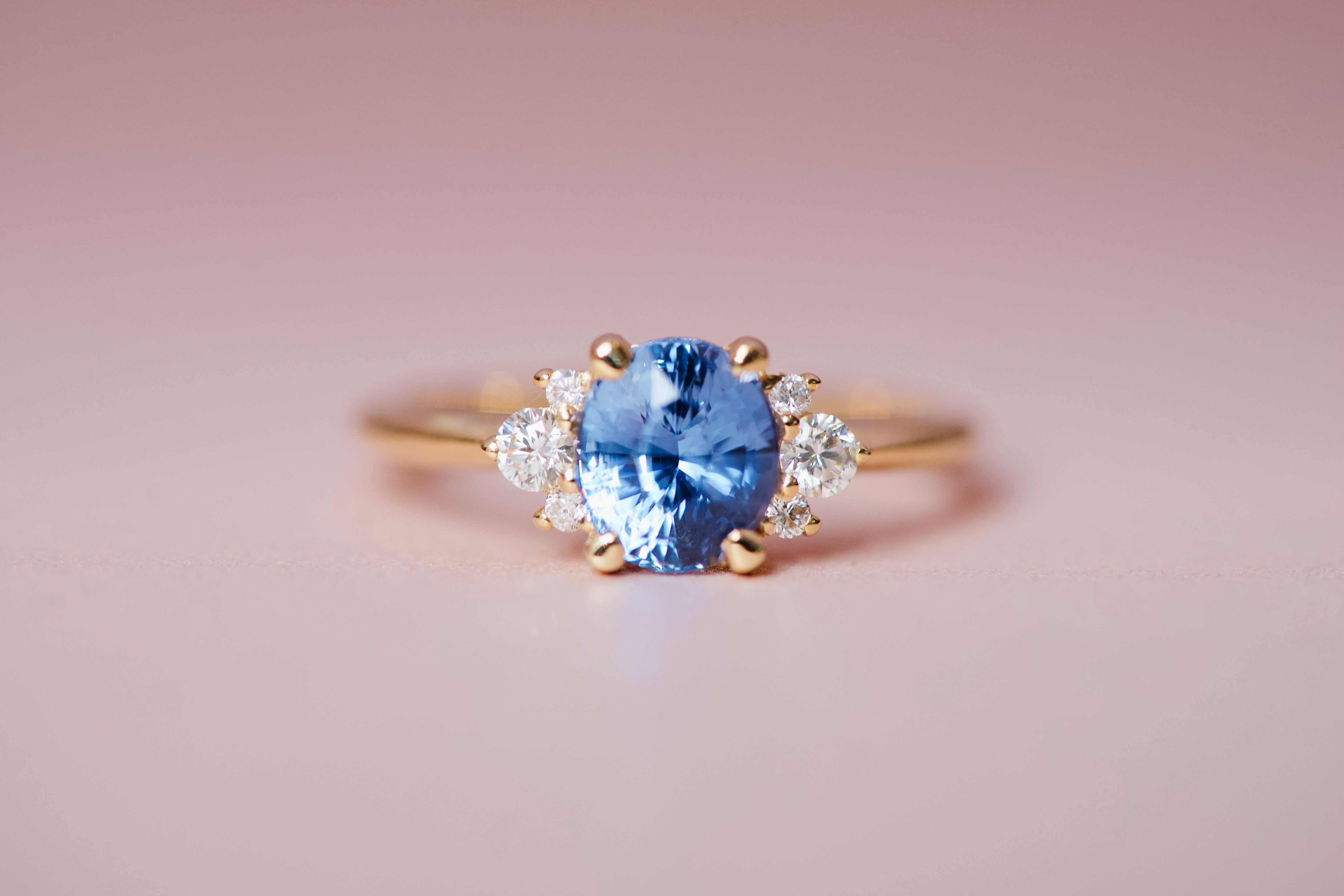 Wide shot of a blue sapphire engagement ring upgrade with small diamond accents on a pink background